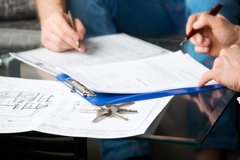A Man is Writing on a Clipboard Next to a Bunch of Papers and Keys — Paton Hooke Lawyers & Conveyancers In Nabiac, NSW
