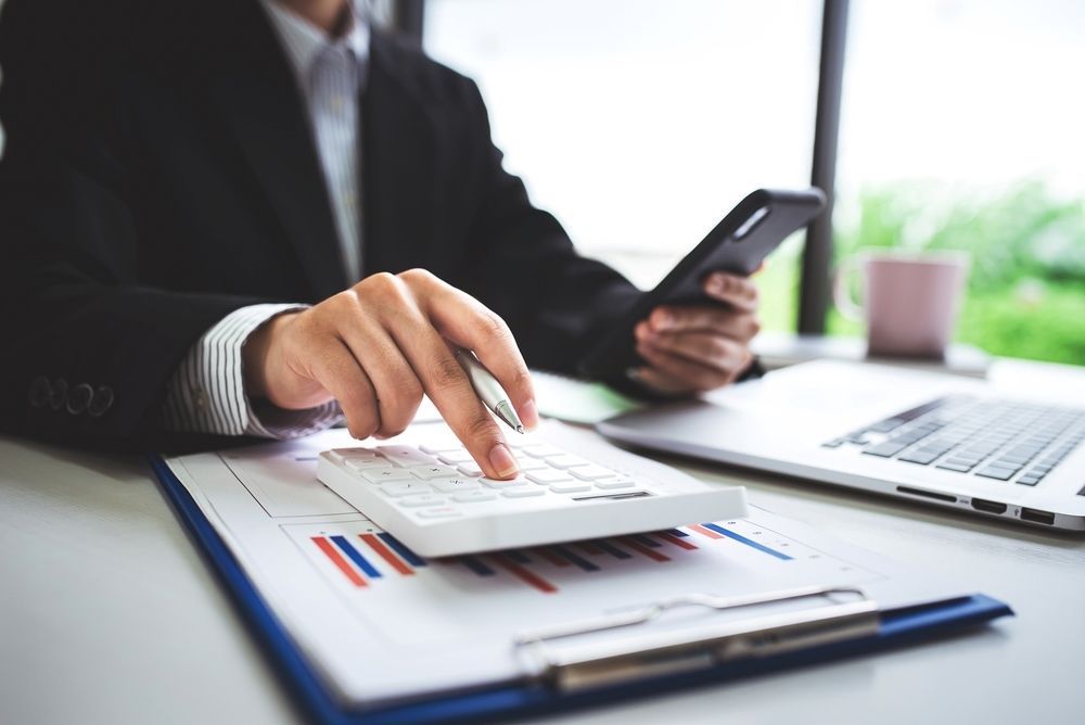 A Man is Using a Calculator While Holding a Cell Phone — Paton Hooke Lawyers & Conveyancers In Taree, NSW