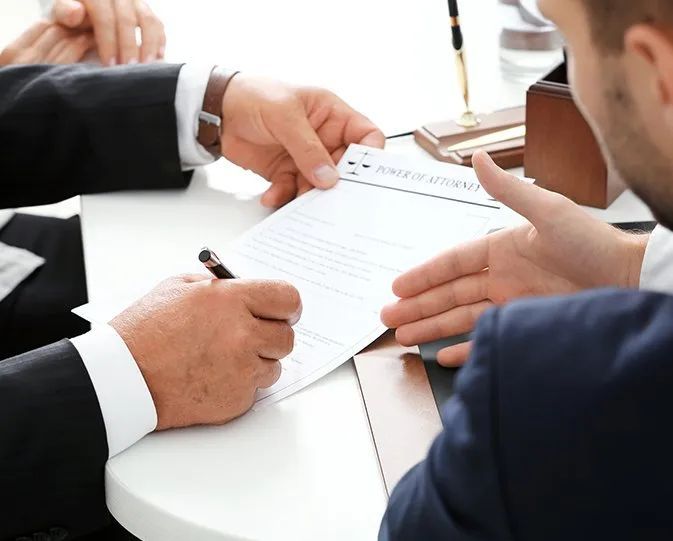 Two Men Are Sitting at a Table Signing a Document — Paton Hooke Lawyers & Conveyancers In Taree, NSW