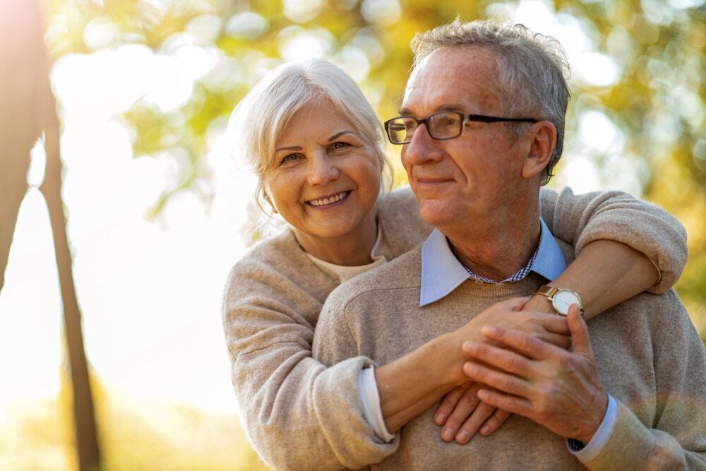 Senior couple embracing outdoors; woman smiling, wrapping arms around man with glasses. — Paton Hooke Lawyers & Conveyancers In Taree, NSW