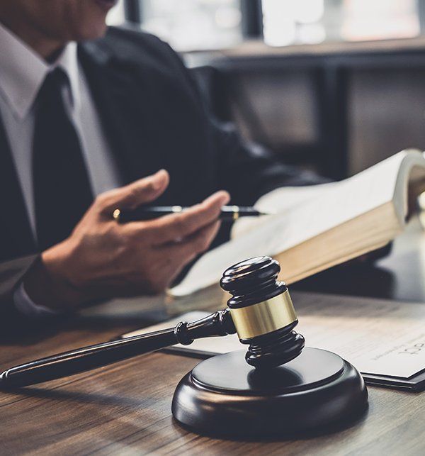 A Man is Sitting at a Table With a Book and a Judge's Gavel — Paton Hooke Lawyers & Conveyancers In Taree, NSW