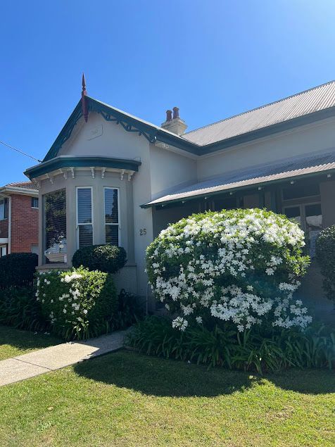 A White House With a Green Roof and White Flowers in Front of It — Paton Hooke Lawyers & Conveyancers In Taree, NSW