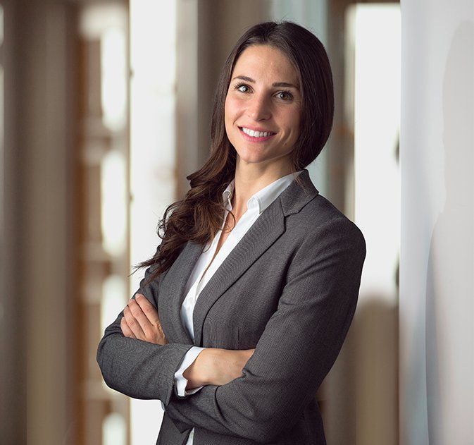 A Woman in a Suit is Standing With Her Arms Crossed and Smiling — Paton Hooke Lawyers & Conveyancers In Wingham, NSW