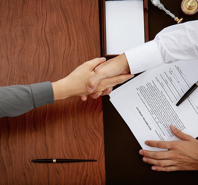 A Man and a Woman Are Shaking Hands Over a Piece of Paper — Paton Hooke Lawyers & Conveyancers In Taree, NSW