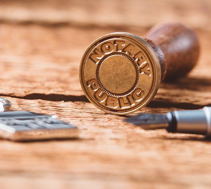 A Gold Notary Public Stamp is Sitting on a Wooden Table Next to a Pen — Paton Hooke Lawyers & Conveyancers In Taree, NSW