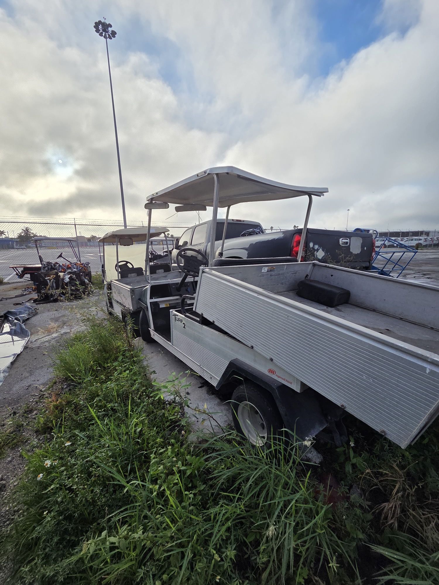 Utility vehicle with a silver bed, parked outdoors on a grassy area, cloudy sky.
