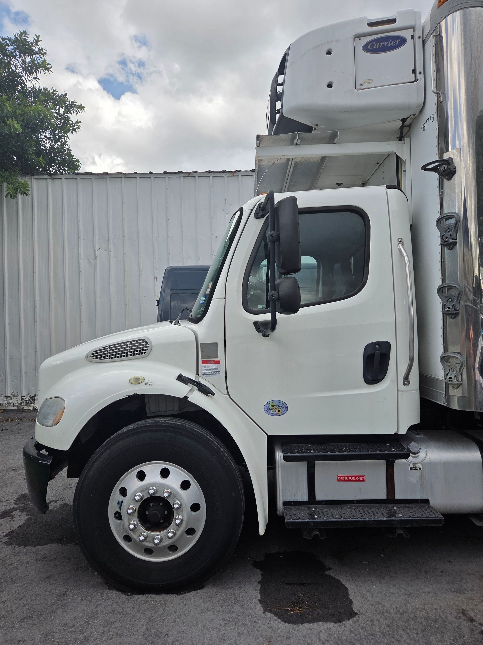 White refrigerated box truck parked, with a Carrier refrigeration unit on top.