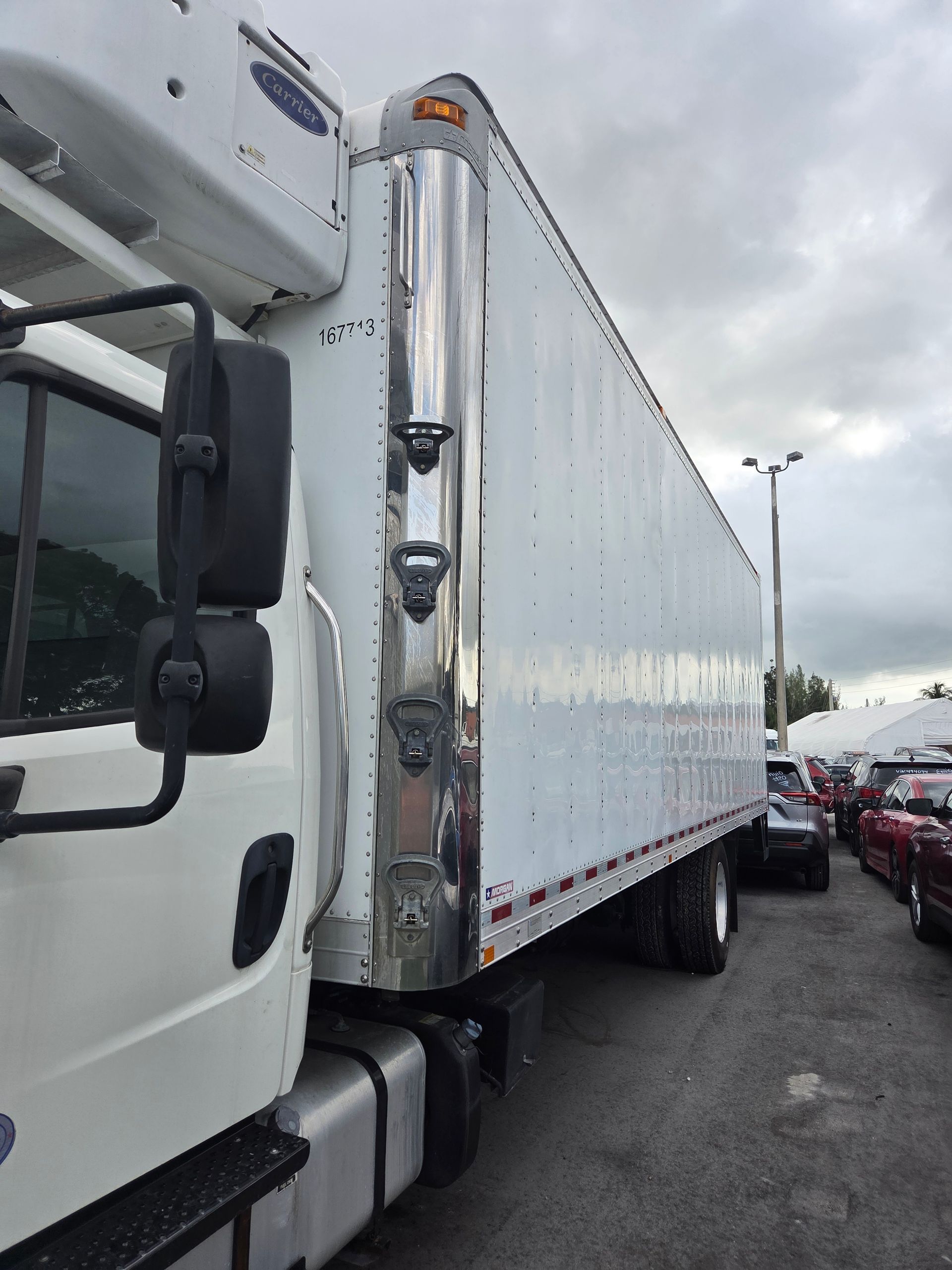White refrigerated truck parked outside, cloudy sky.