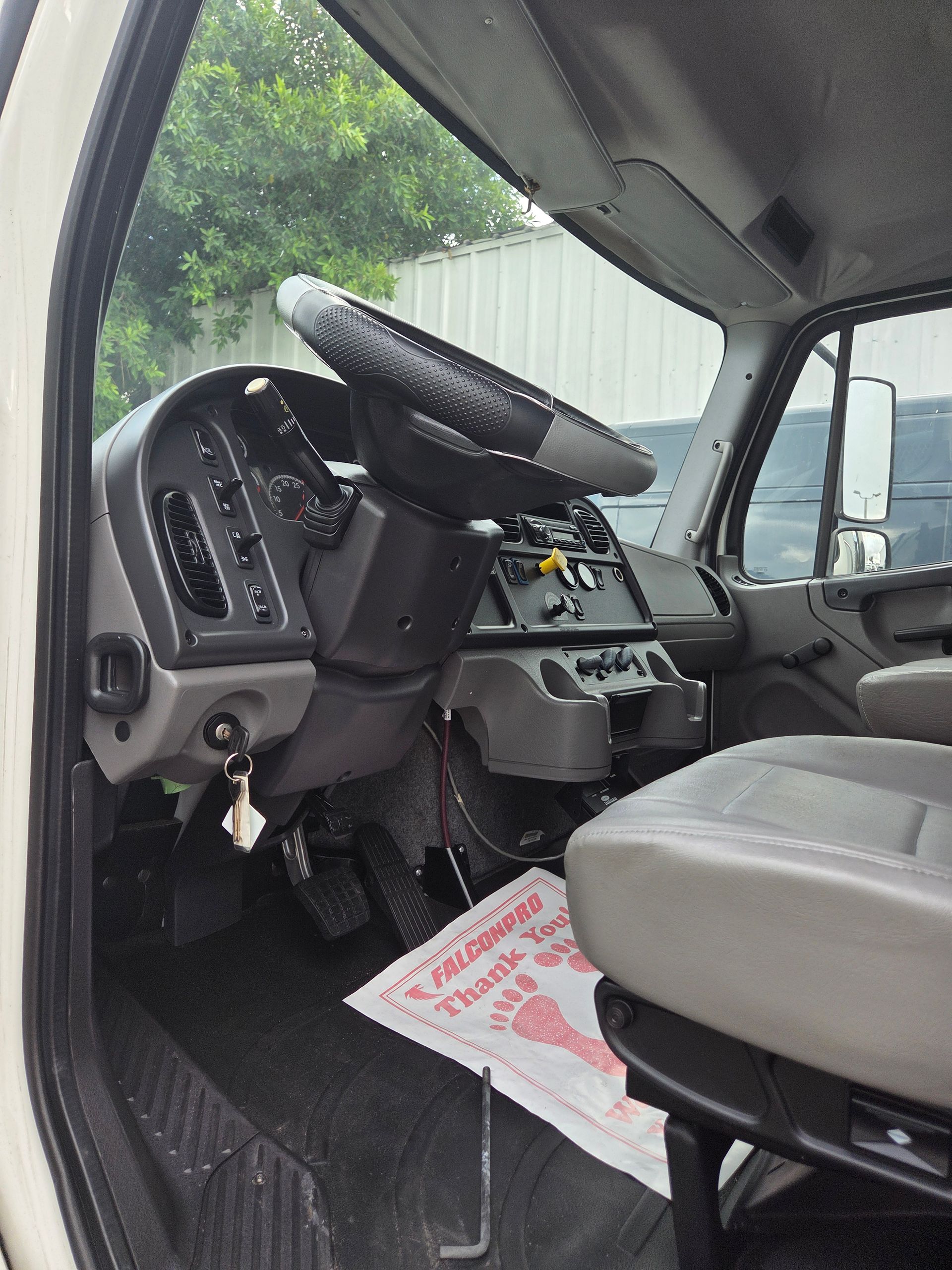 Interior view of a truck cab, showing the steering wheel, dashboard, pedals, and seat.