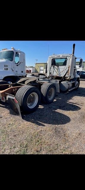 A white semi-truck in a gravel lot on a sunny day. Another truck is partially visible on the left.