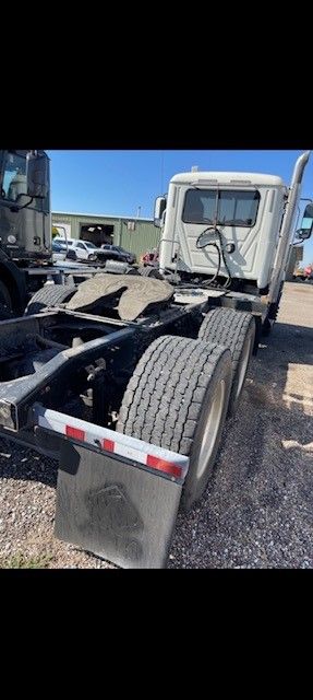 White semi-truck with a black frame on gravel under a blue sky.