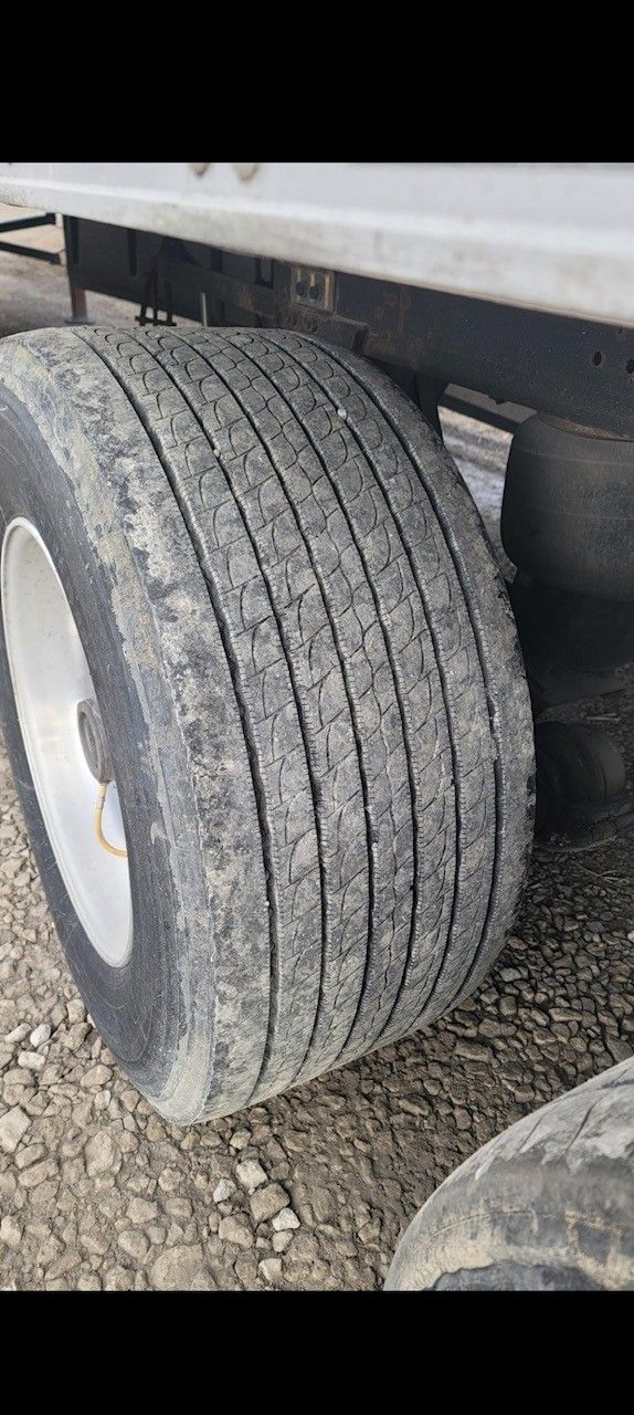 Close-up of a truck tire with visible tread. Tire is dusty, mounted on a silver rim.