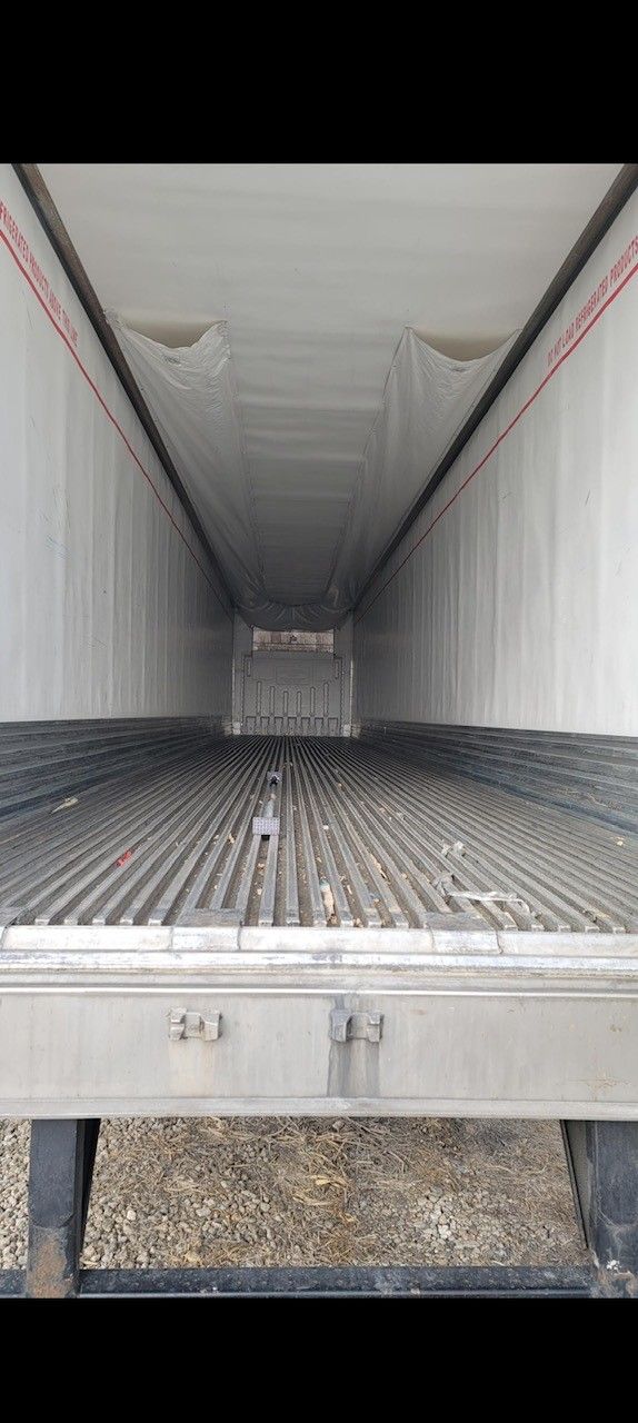 Inside of an empty refrigerated semi-trailer, gray floor, white walls and ceiling, perspective view.
