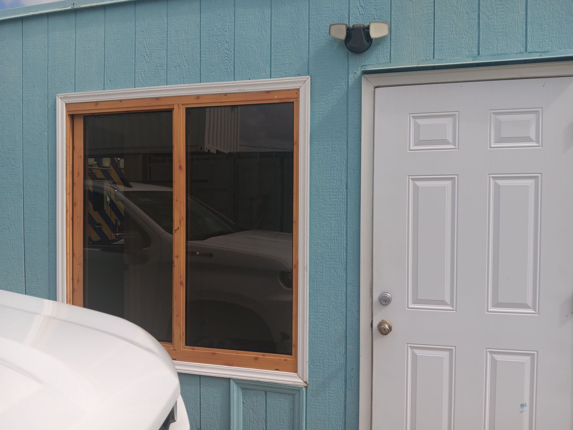 Blue building with window and white door; car partially visible.