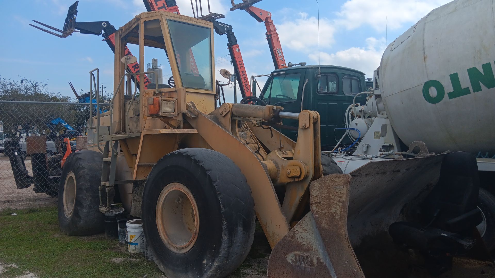 Yellow front-end loader next to a concrete mixer truck and black SUV, outdoors under a cloudy sky.