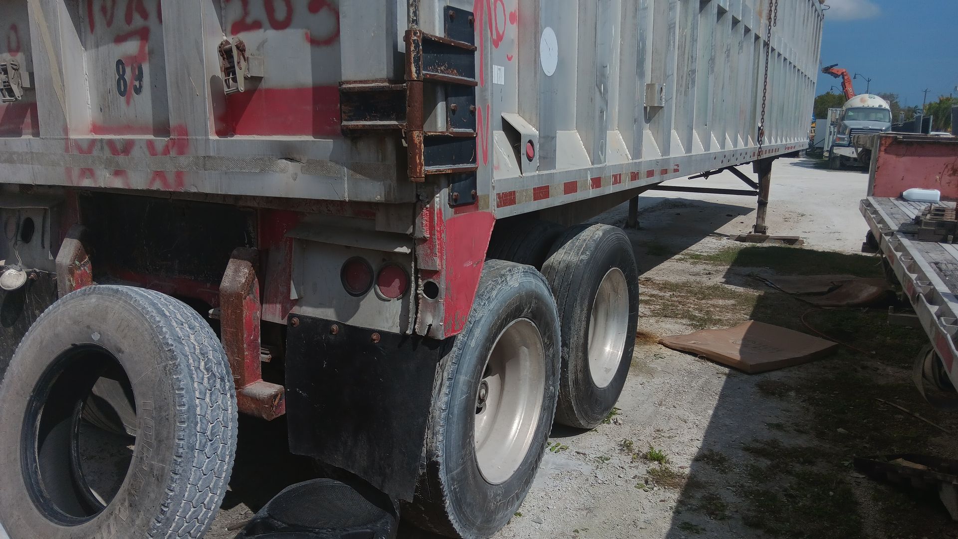 Semi-trailer with dual tires; spare tire on the ground, red and silver; outdoors.