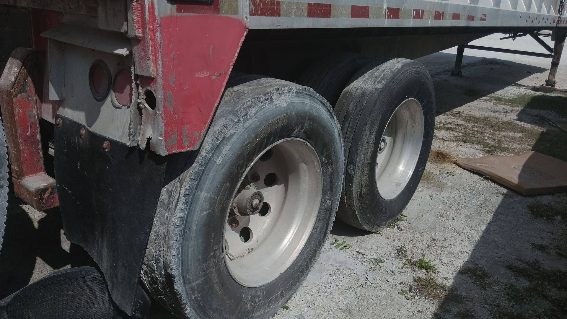 Close-up of a semi-trailer's dual wheels, covered in white material, parked on concrete.