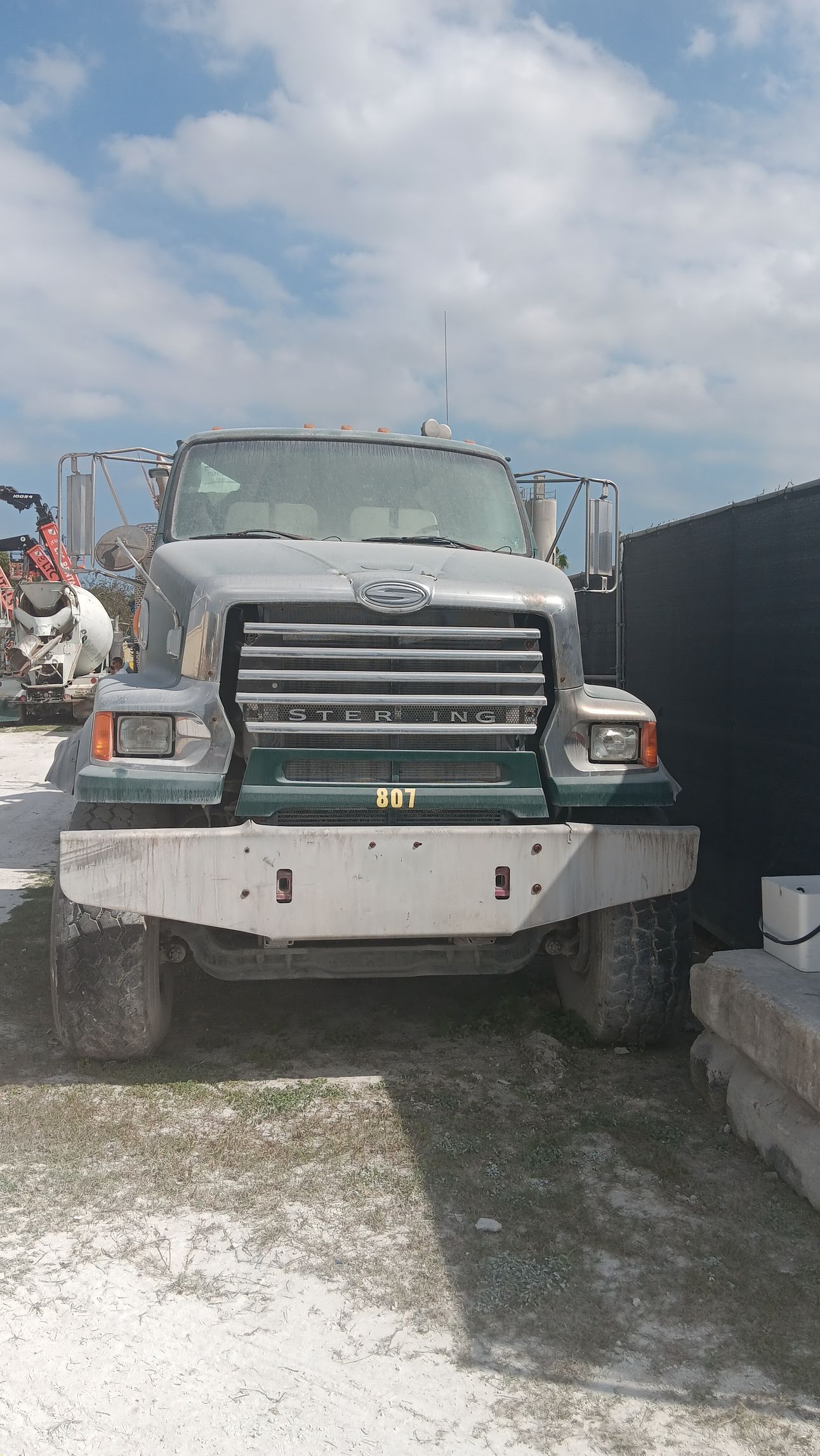 Green and gray truck parked in an outdoor area, facing forward. White ground. Blue sky.