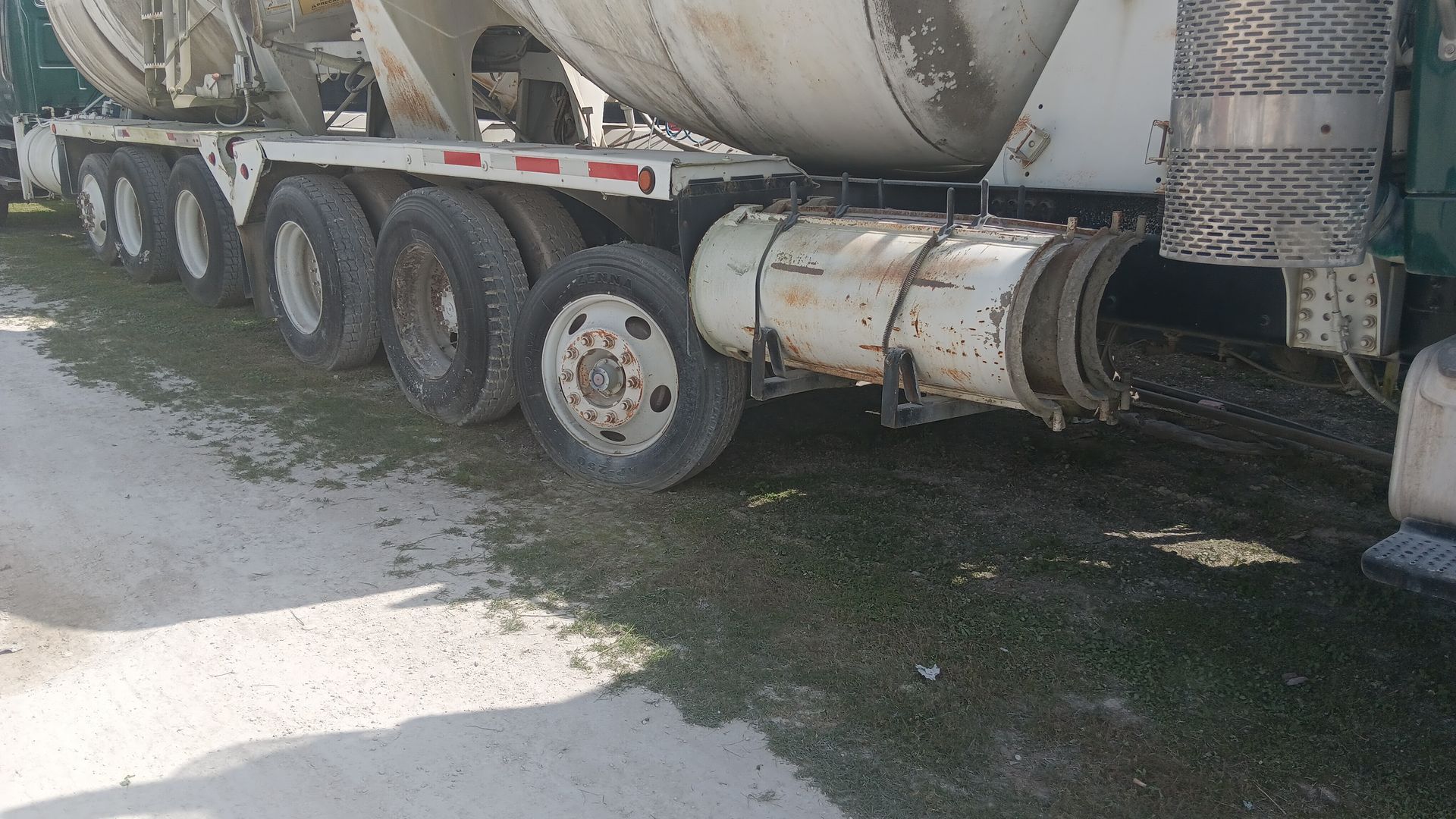 A cement truck parked on a dirt road with grass.