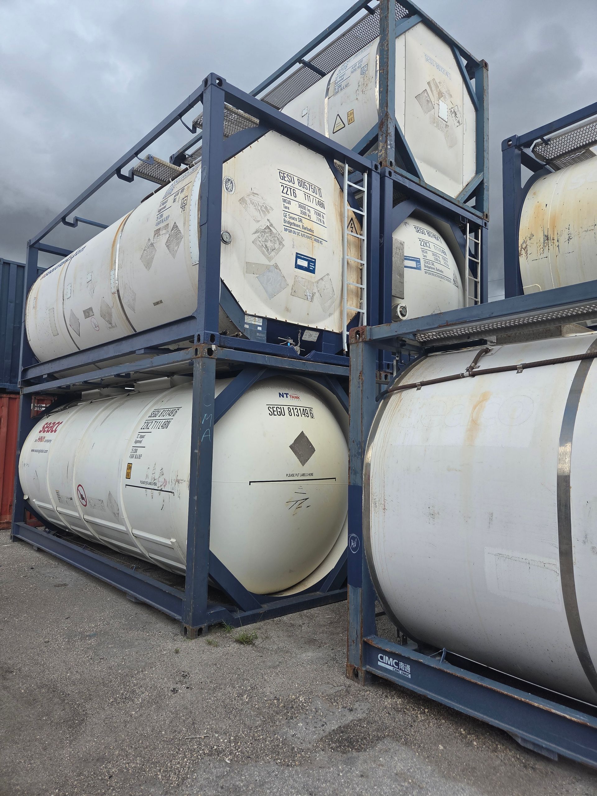 Stacked white tank containers in blue frames, outdoors.