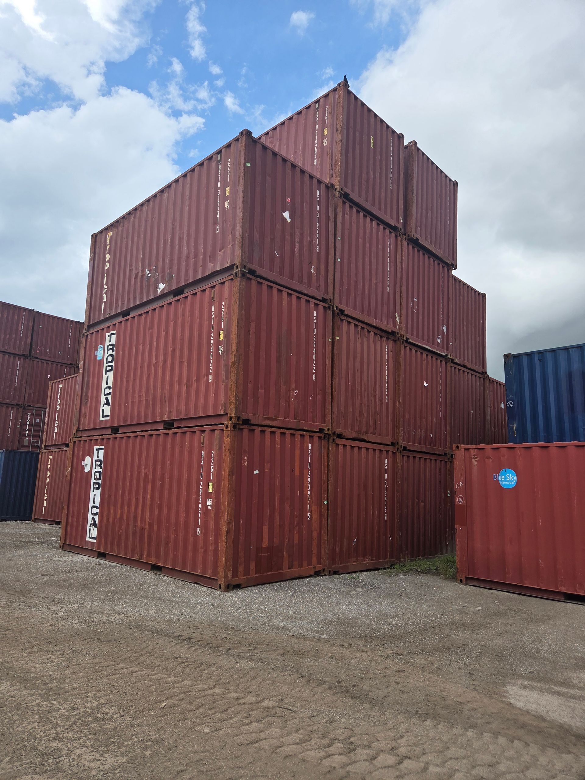 Red shipping containers stacked outdoors under a cloudy sky.