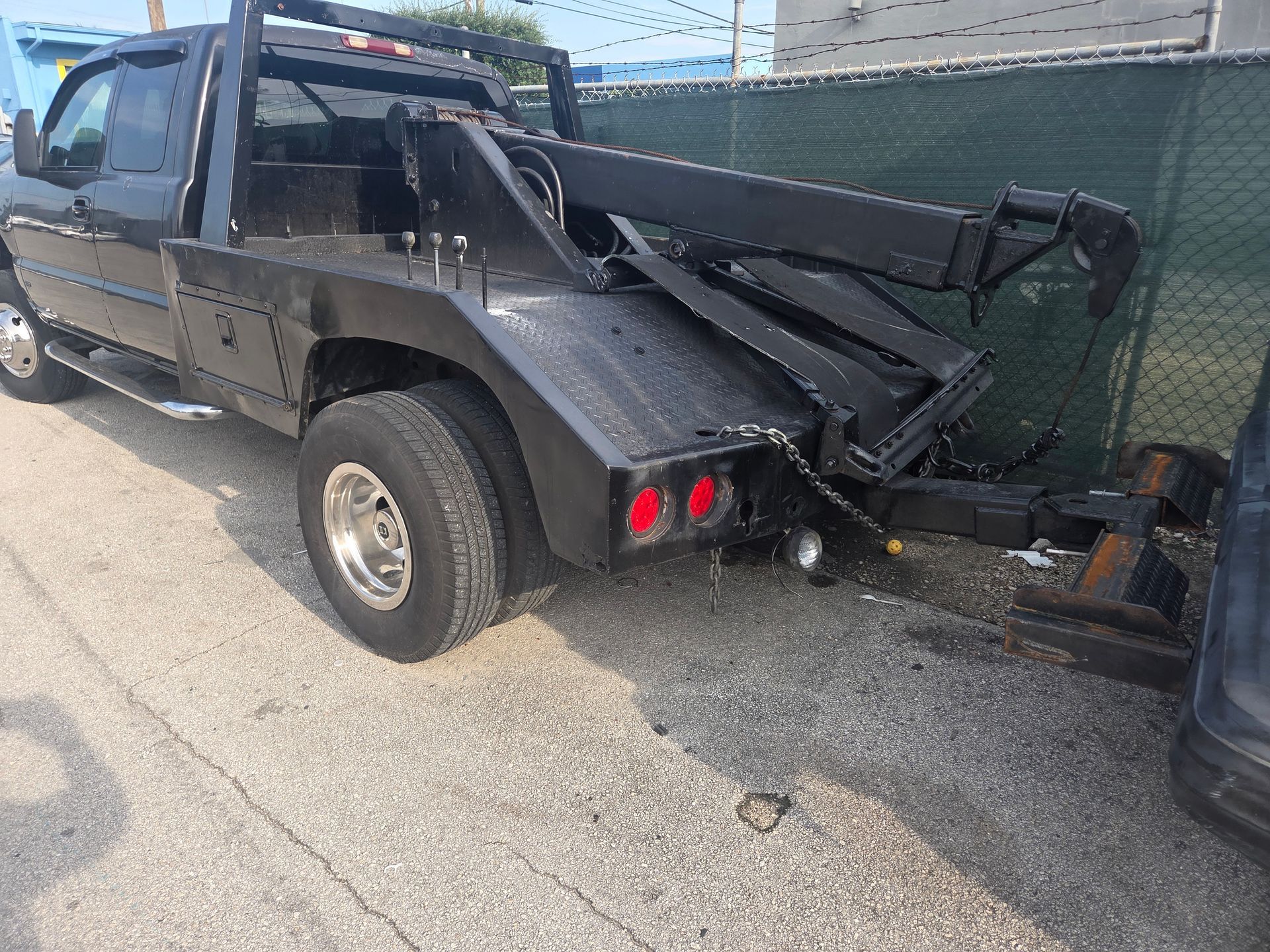 Black tow truck parked outside, rear view showing the tow lift and red taillights.