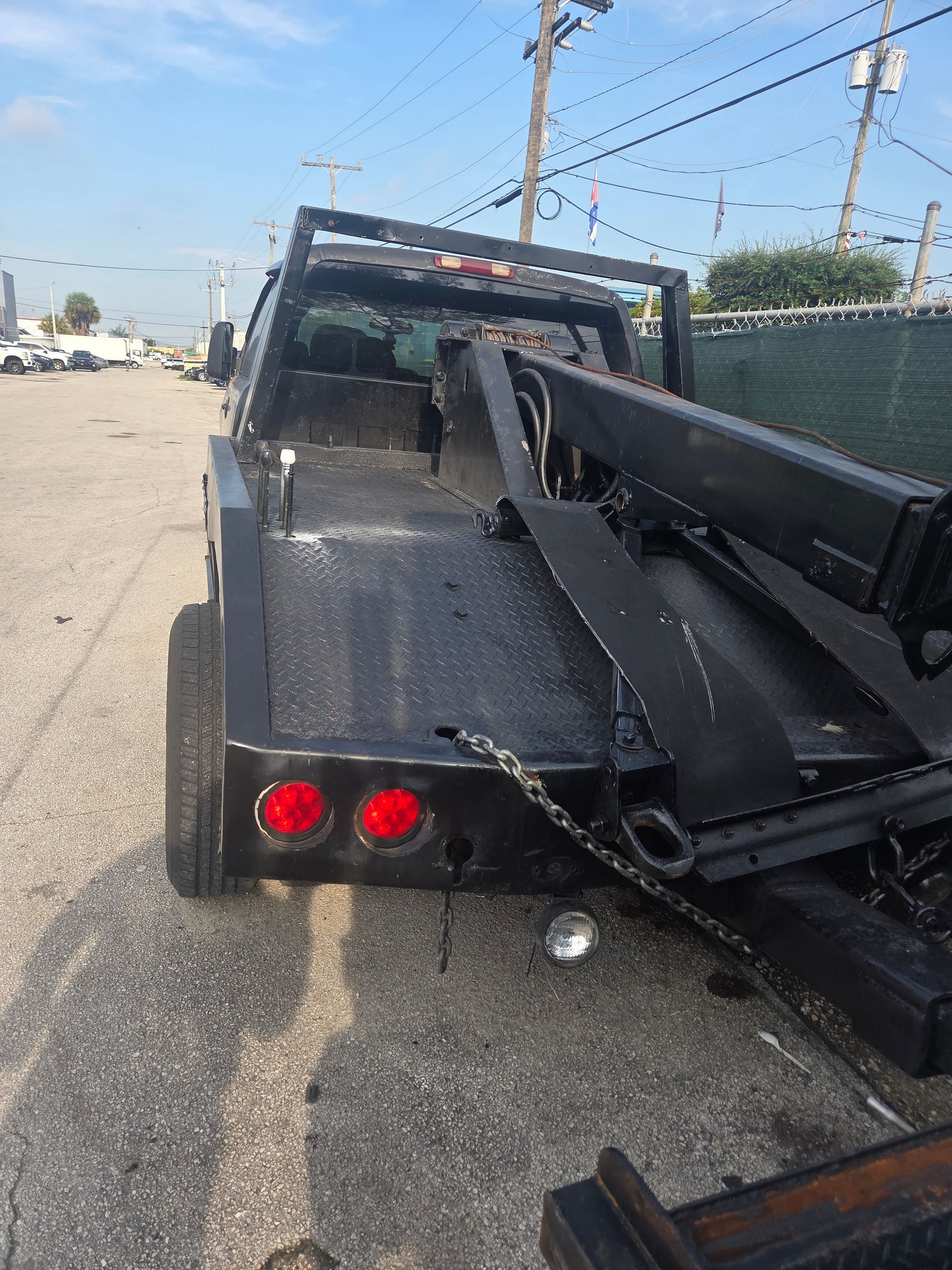 Black tow truck on a paved road; rear view. Red taillights visible. Day time, outdoors.