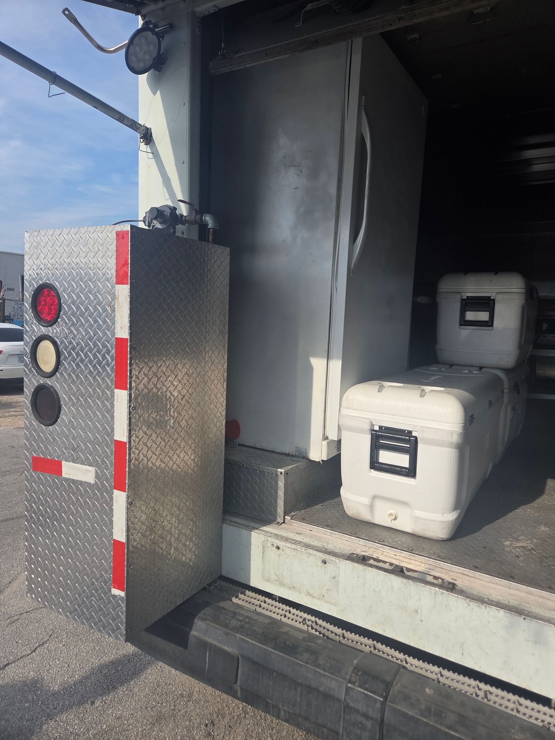 Truck interior with white coolers, a metal box with lights, and a metal refrigerator.