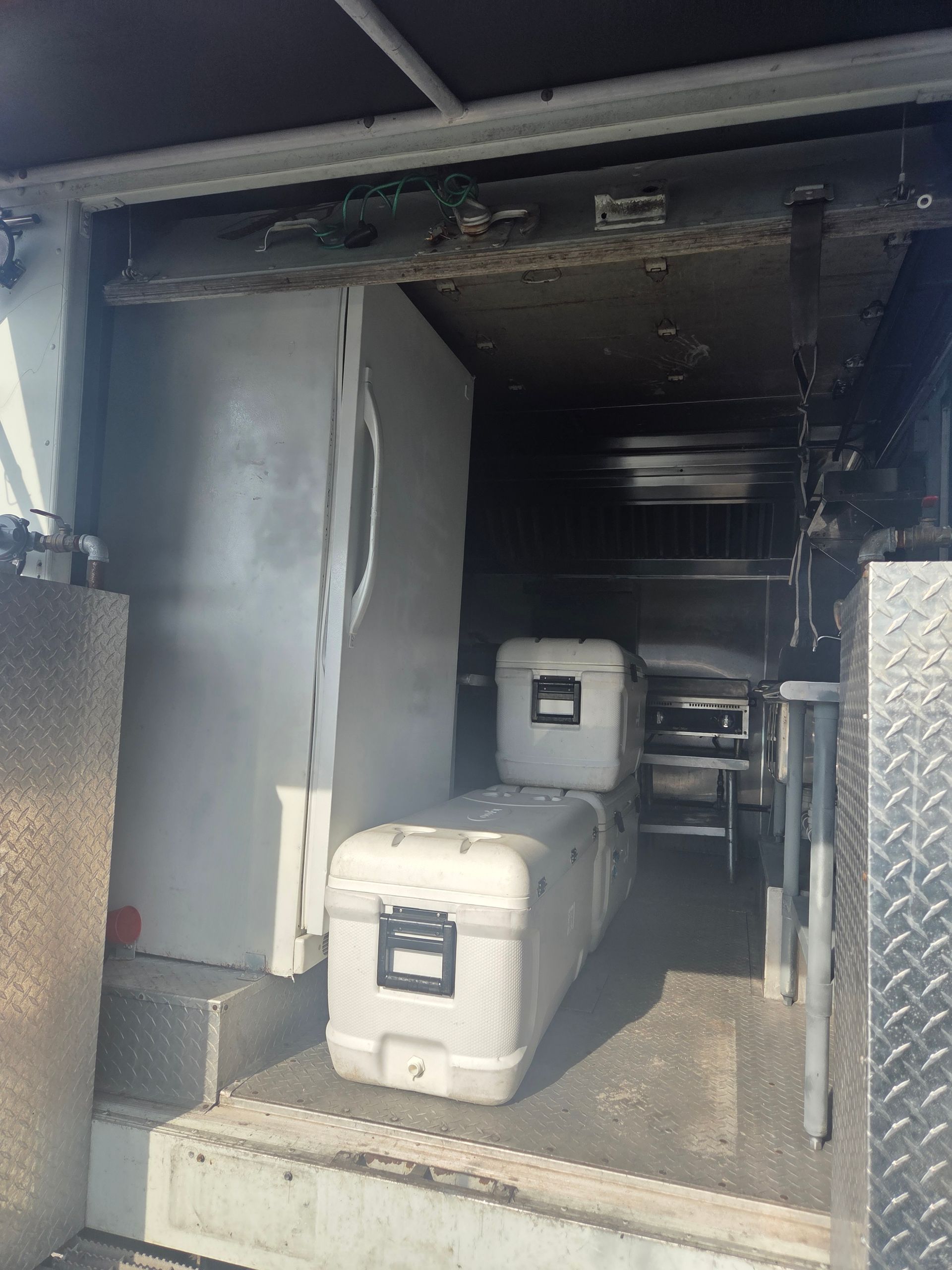 Interior of a vehicle; large refrigerator, white storage containers, and metal shelving.