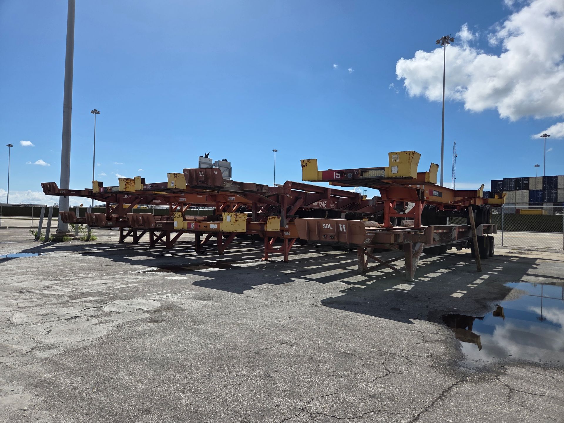 Empty shipping container chassis in a paved lot, under a blue sky.