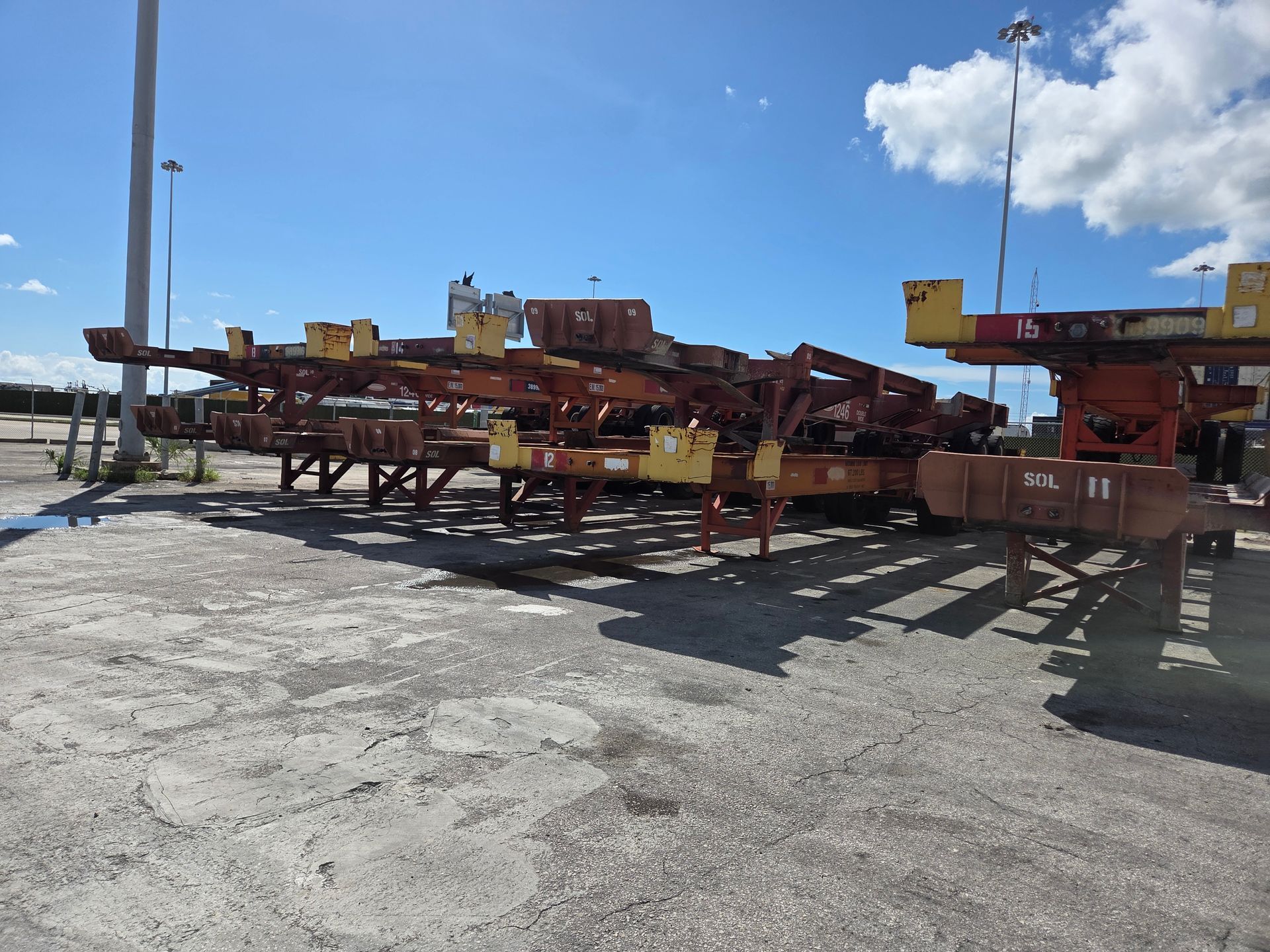 Several rusty container chassis parked on a gravel lot under a blue sky.