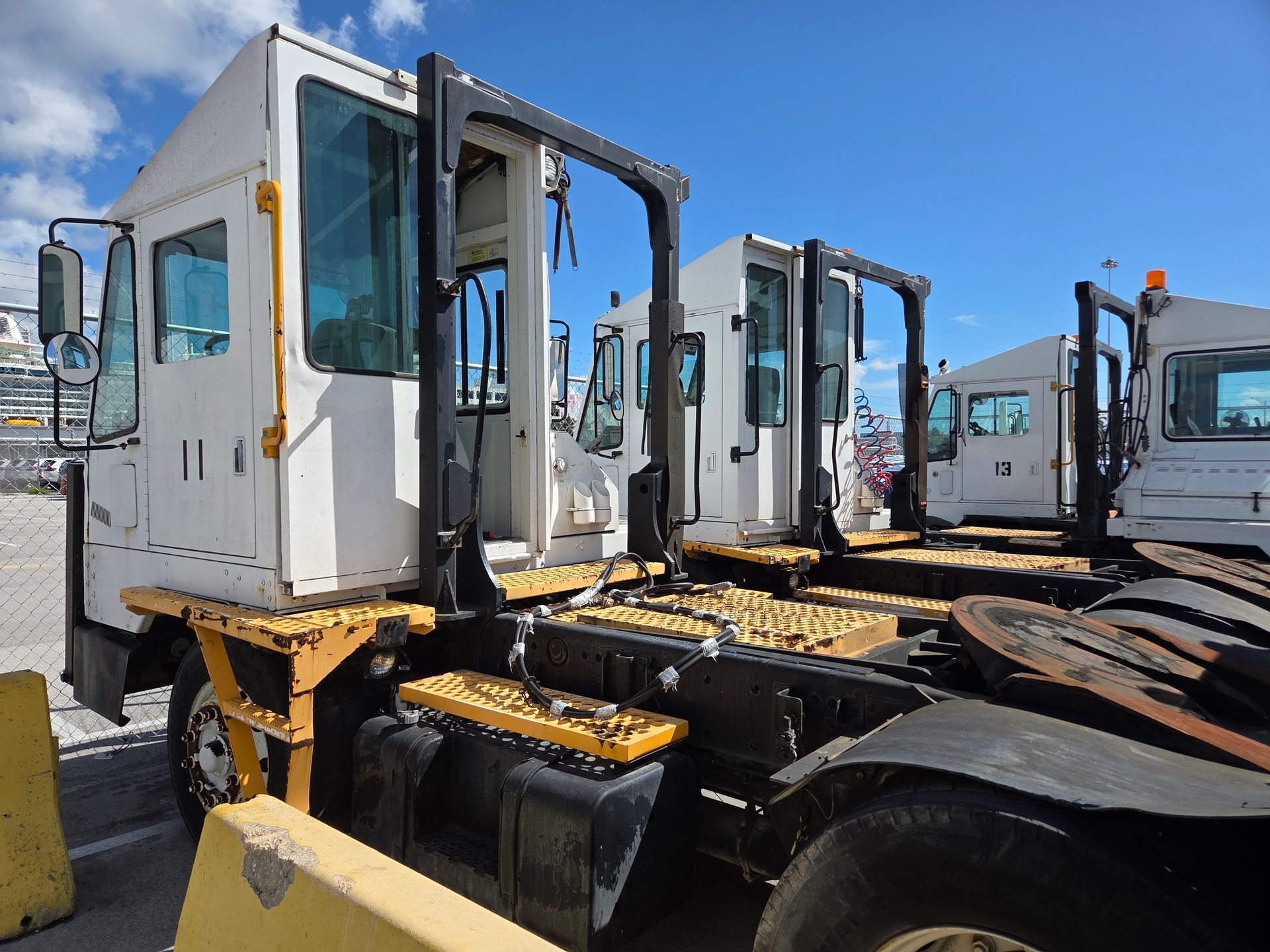 White semi-trucks with black frames parked outside, yellow accents, against a blue sky.