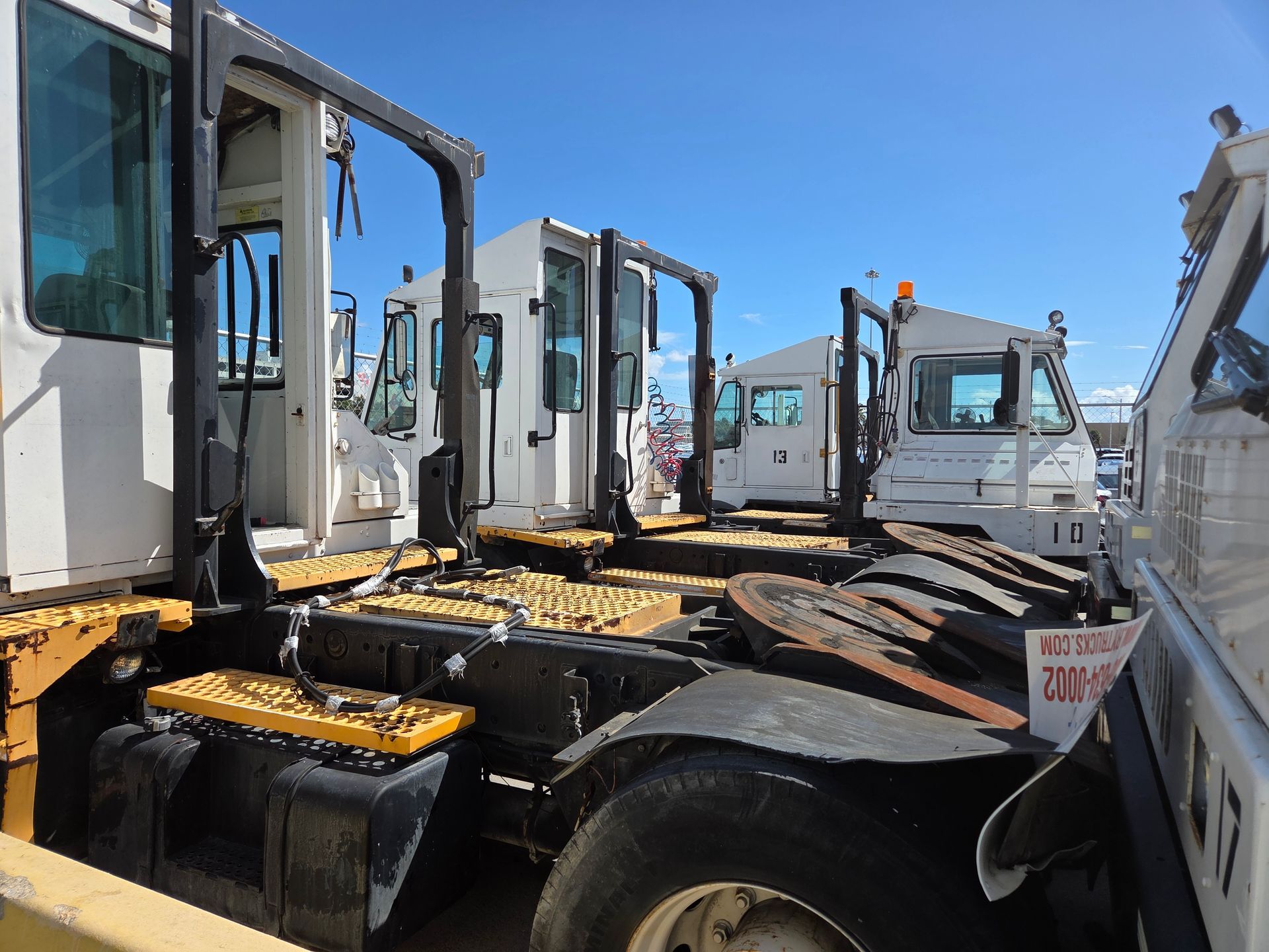 Several white airport tow tractors parked outdoors on a sunny day.