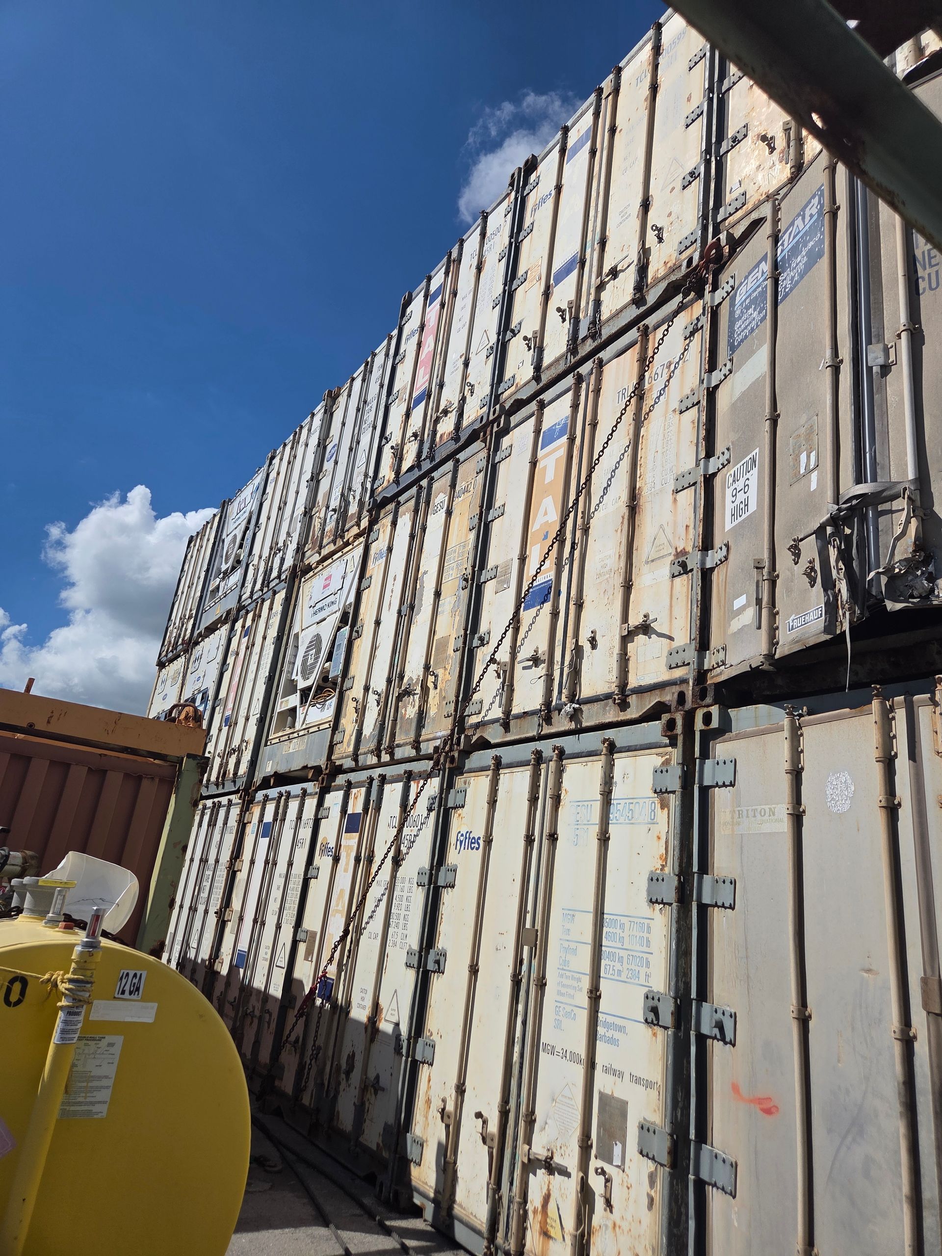 Stack of weathered shipping containers against a blue sky.