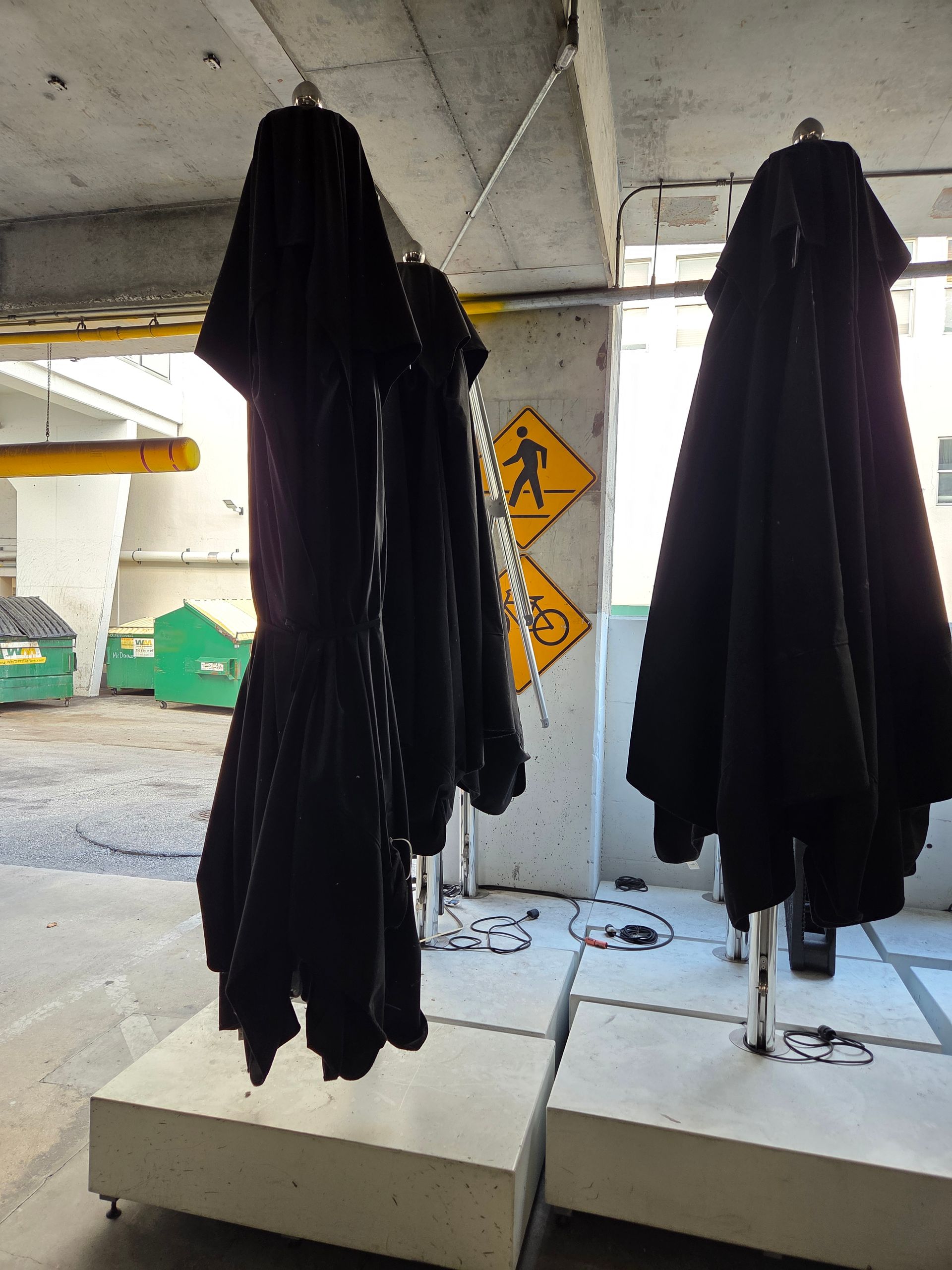 Black umbrellas hanging in a concrete structure, next to a crosswalk sign.