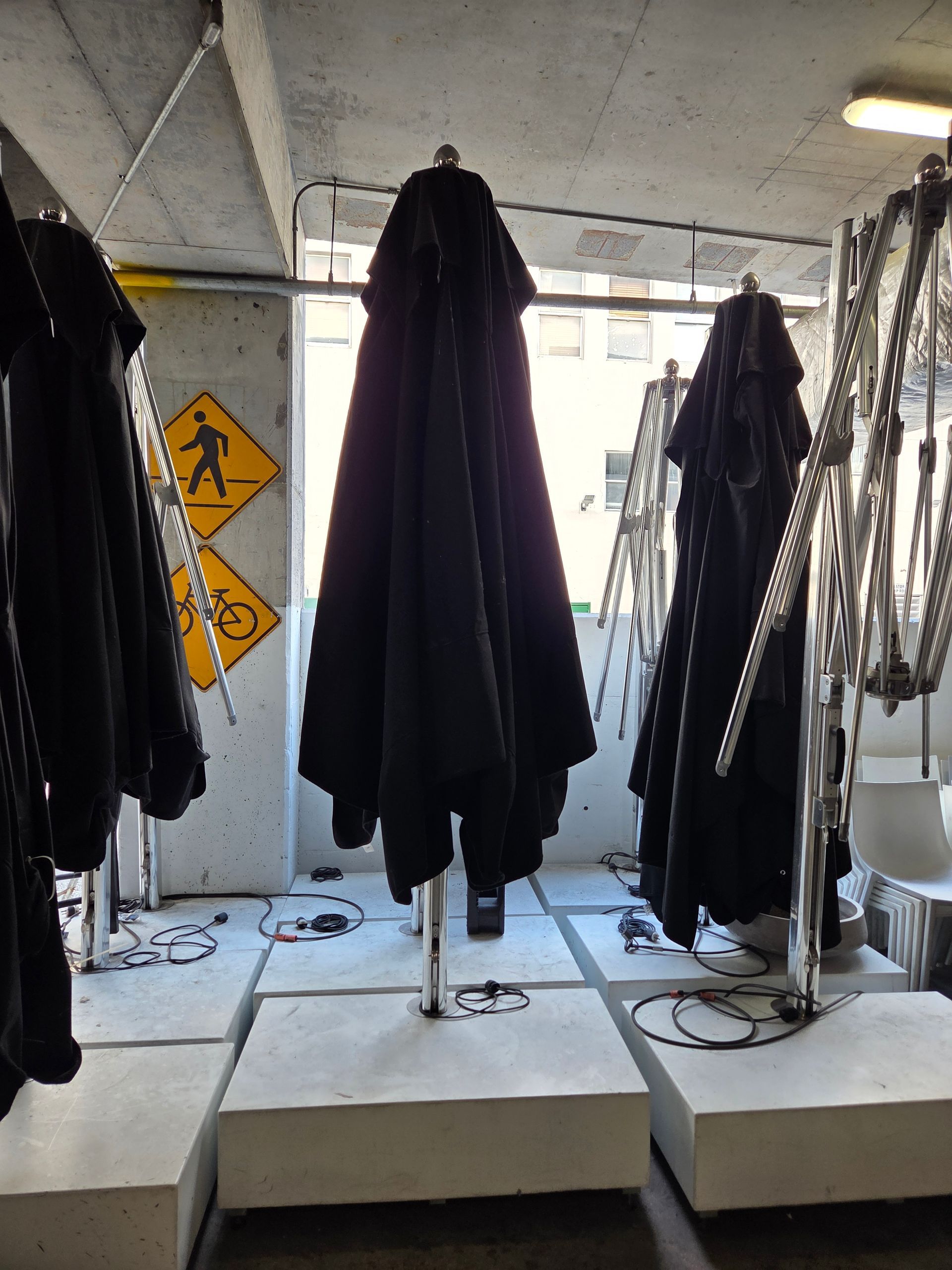 Black umbrellas on concrete pedestals in a room with pedestrian and bike signs.