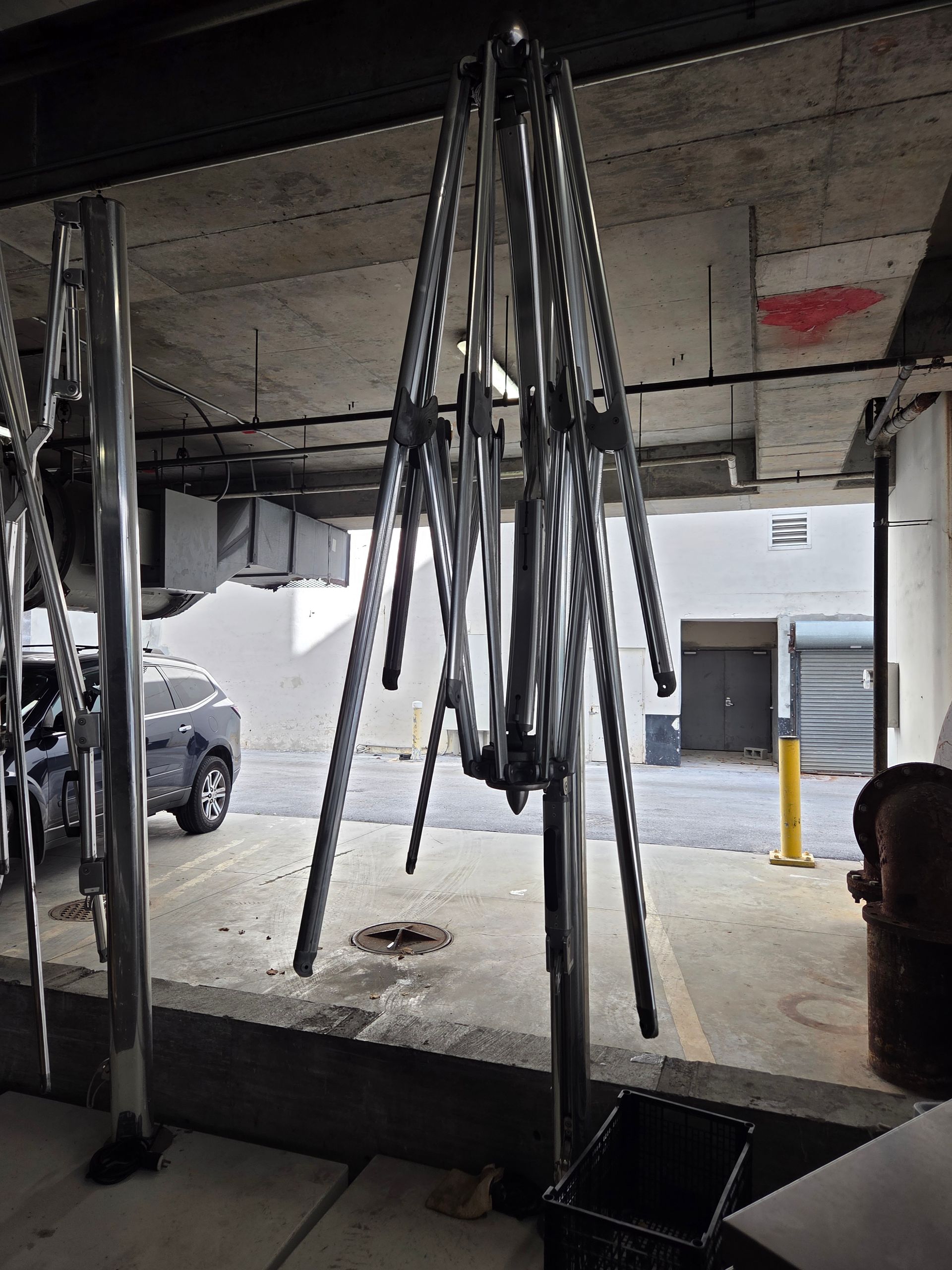 Metal drying rack, hanging in a parking garage. Black, cylindrical supports and gray, metallic structures.