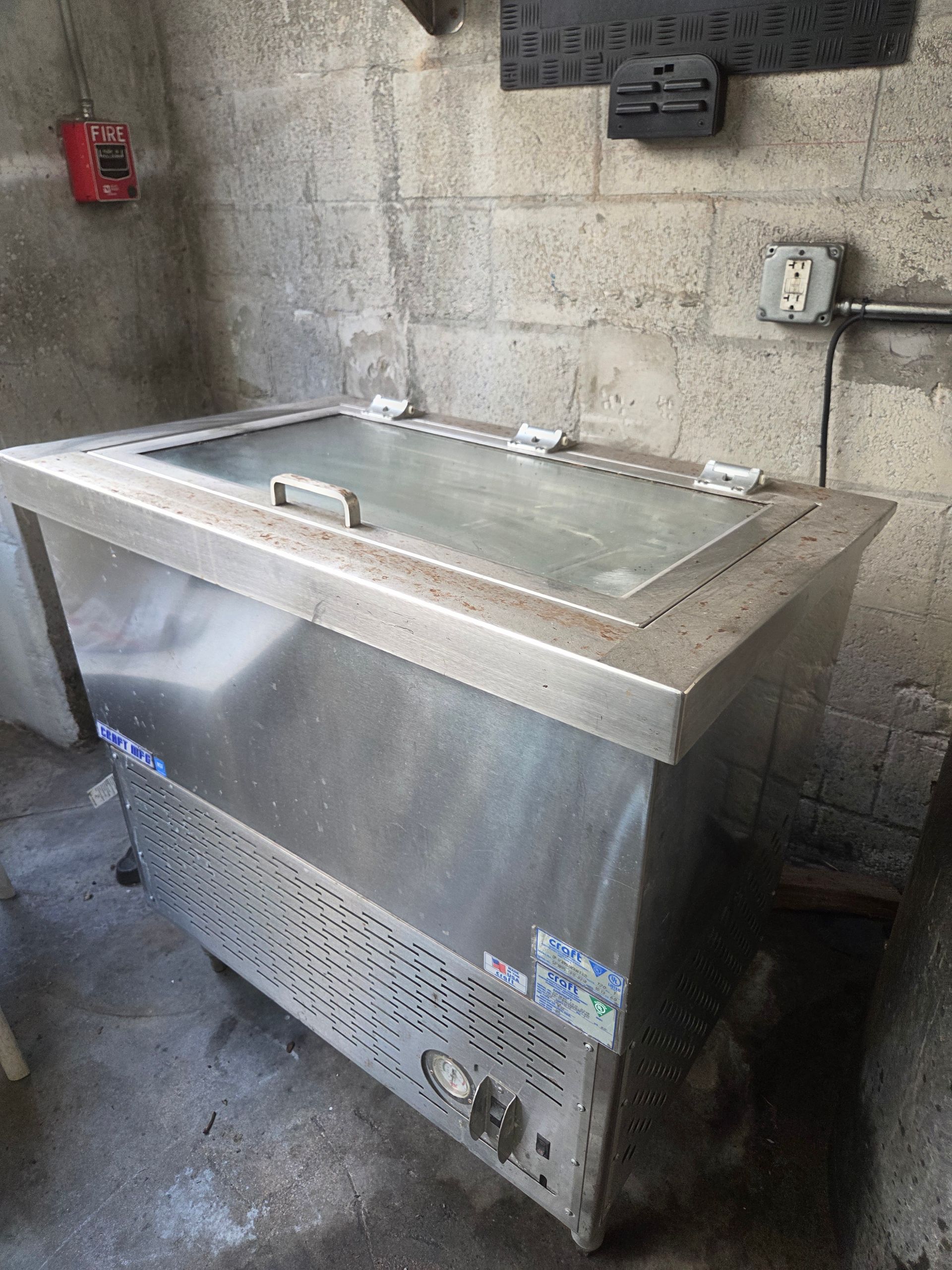 Stainless steel ice cream freezer against a gray concrete wall.