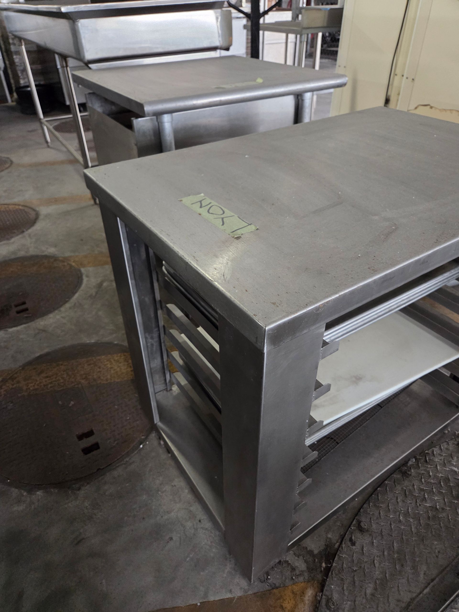 Stainless steel kitchen prep tables with open shelving in an industrial setting.