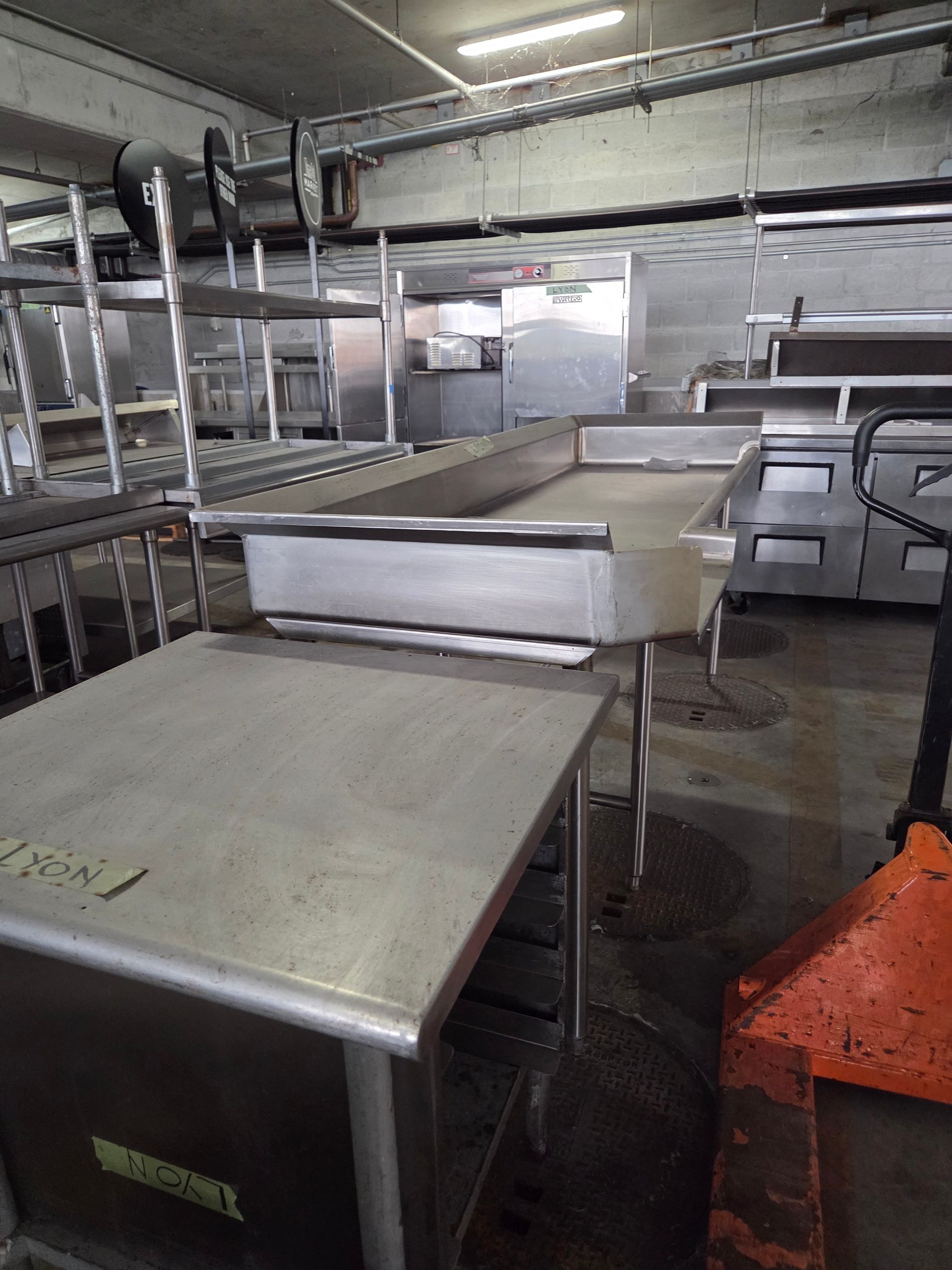 Empty stainless steel commercial kitchen with tables, shelves, and equipment; floor is wet.
