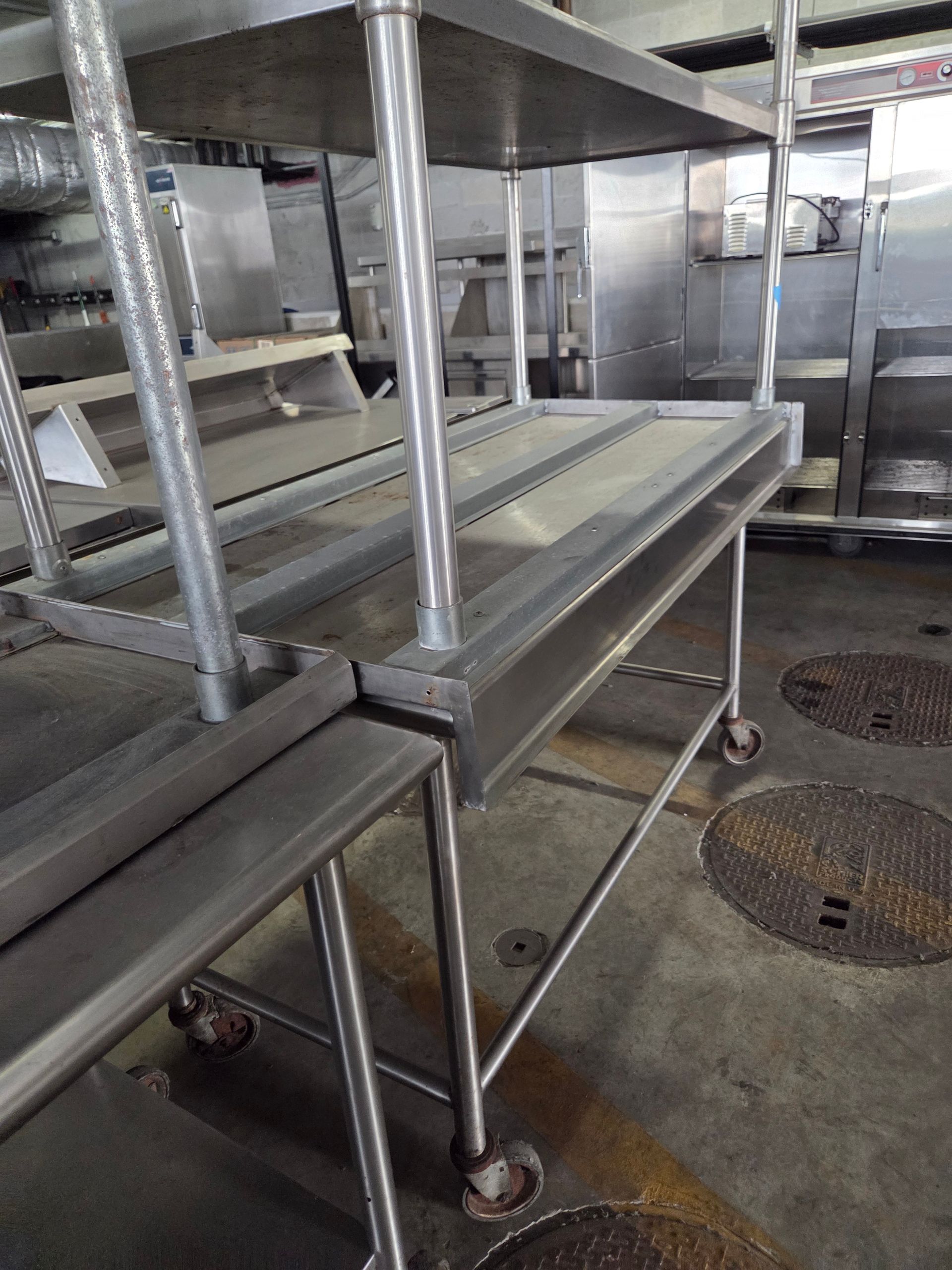 Stainless steel shelving unit with wheels in a commercial kitchen setting.