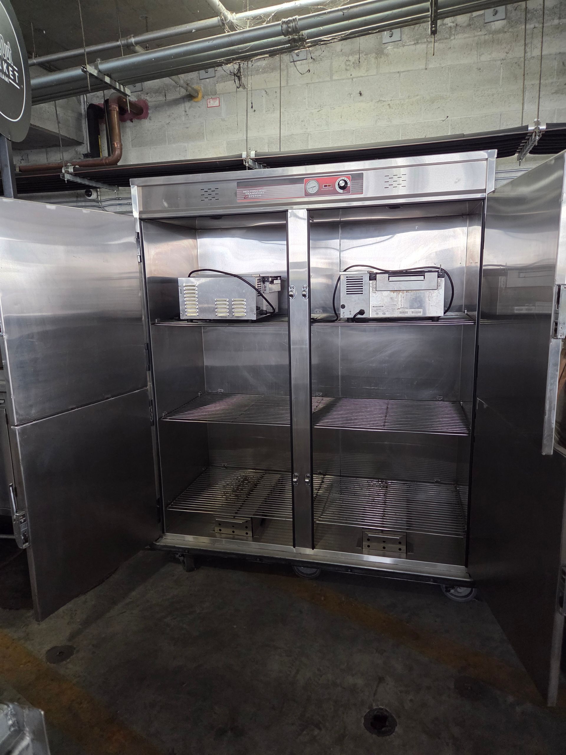 Stainless steel commercial refrigerator with doors open, two shelves, and equipment inside.