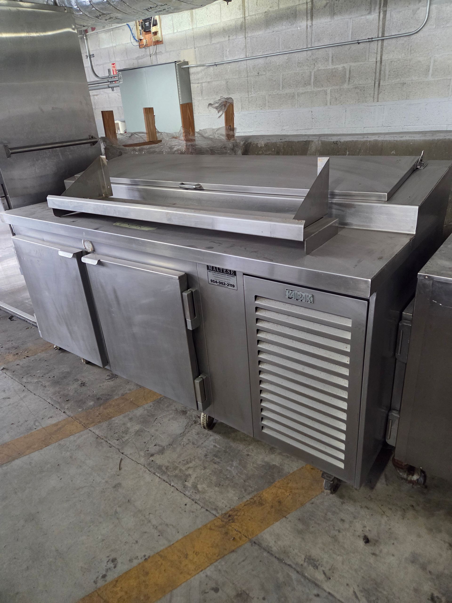 Stainless steel commercial kitchen refrigerator with two doors and a vent, indoors.