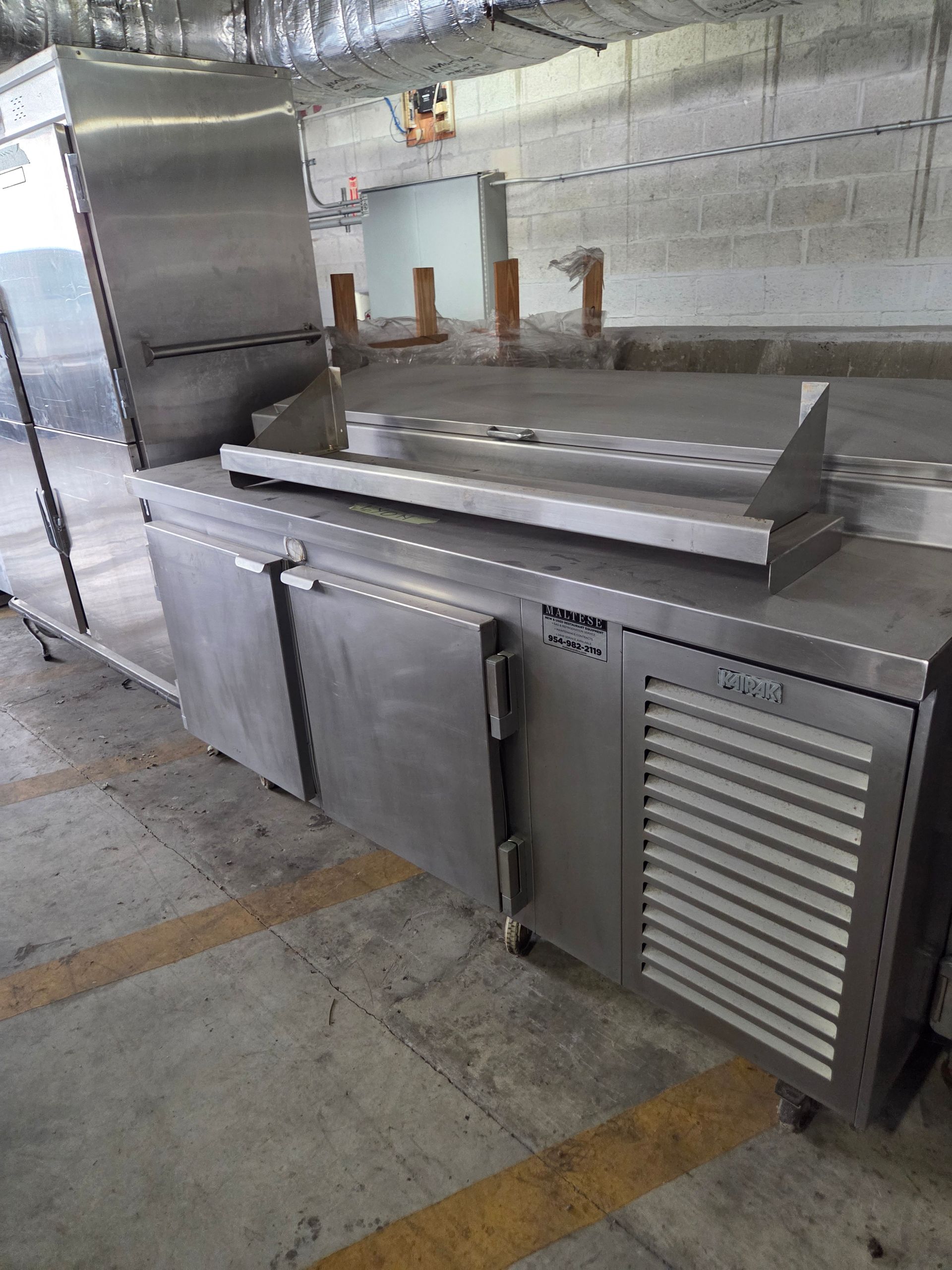 Stainless steel commercial refrigerator and countertop in a warehouse.