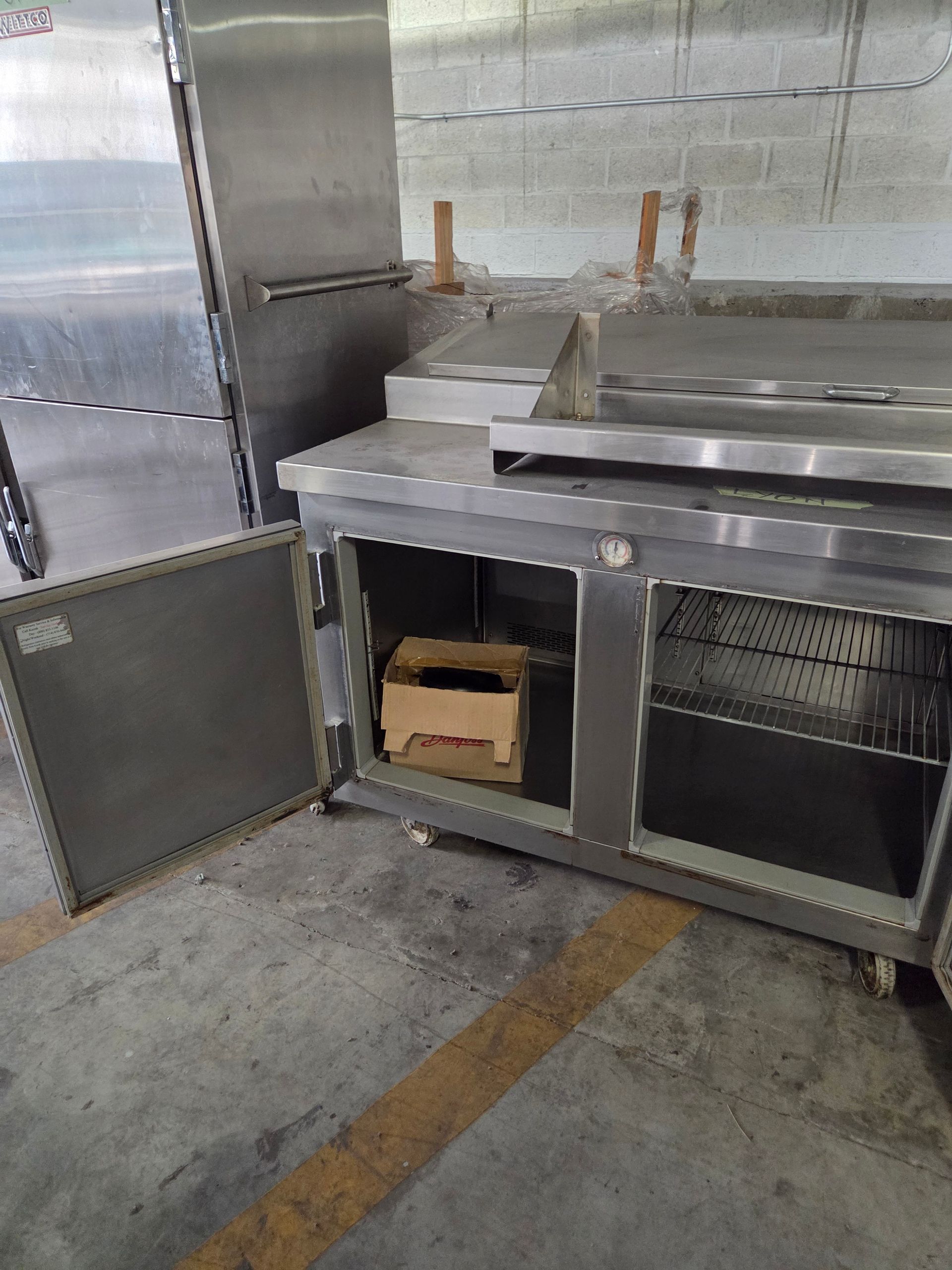 Stainless steel commercial refrigerator with open doors; a box is inside.