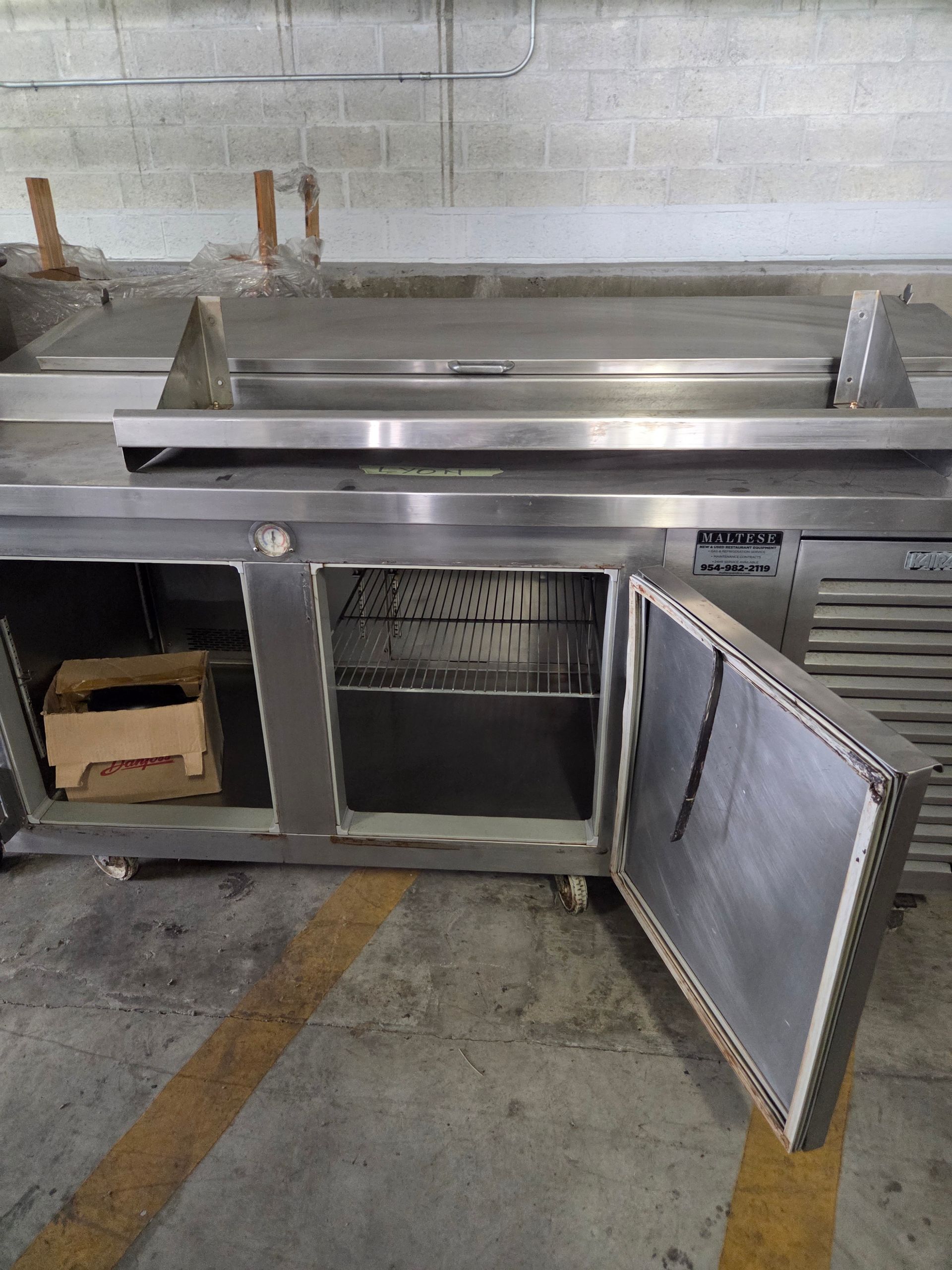 Stainless steel commercial refrigerator with open door, interior shelves, and a cardboard box.
