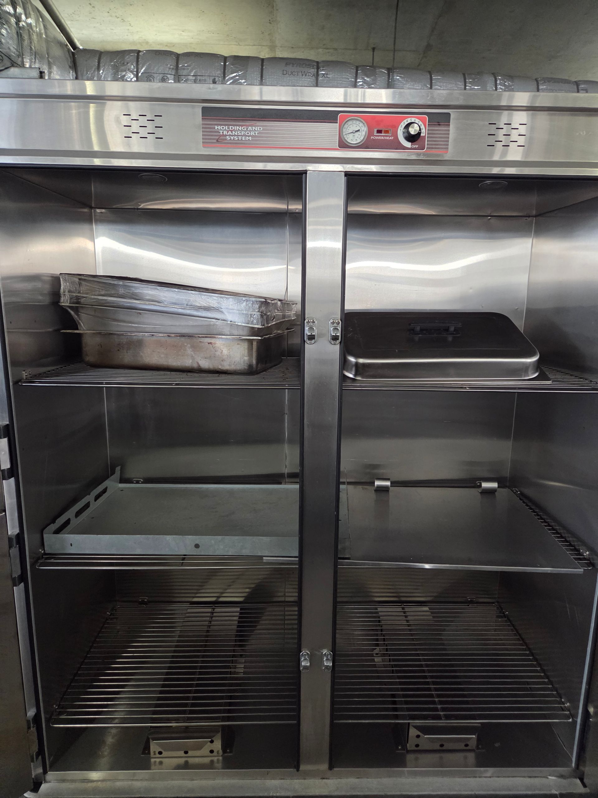 Stainless steel food warmer cabinet with two compartments, trays, and a temperature control.