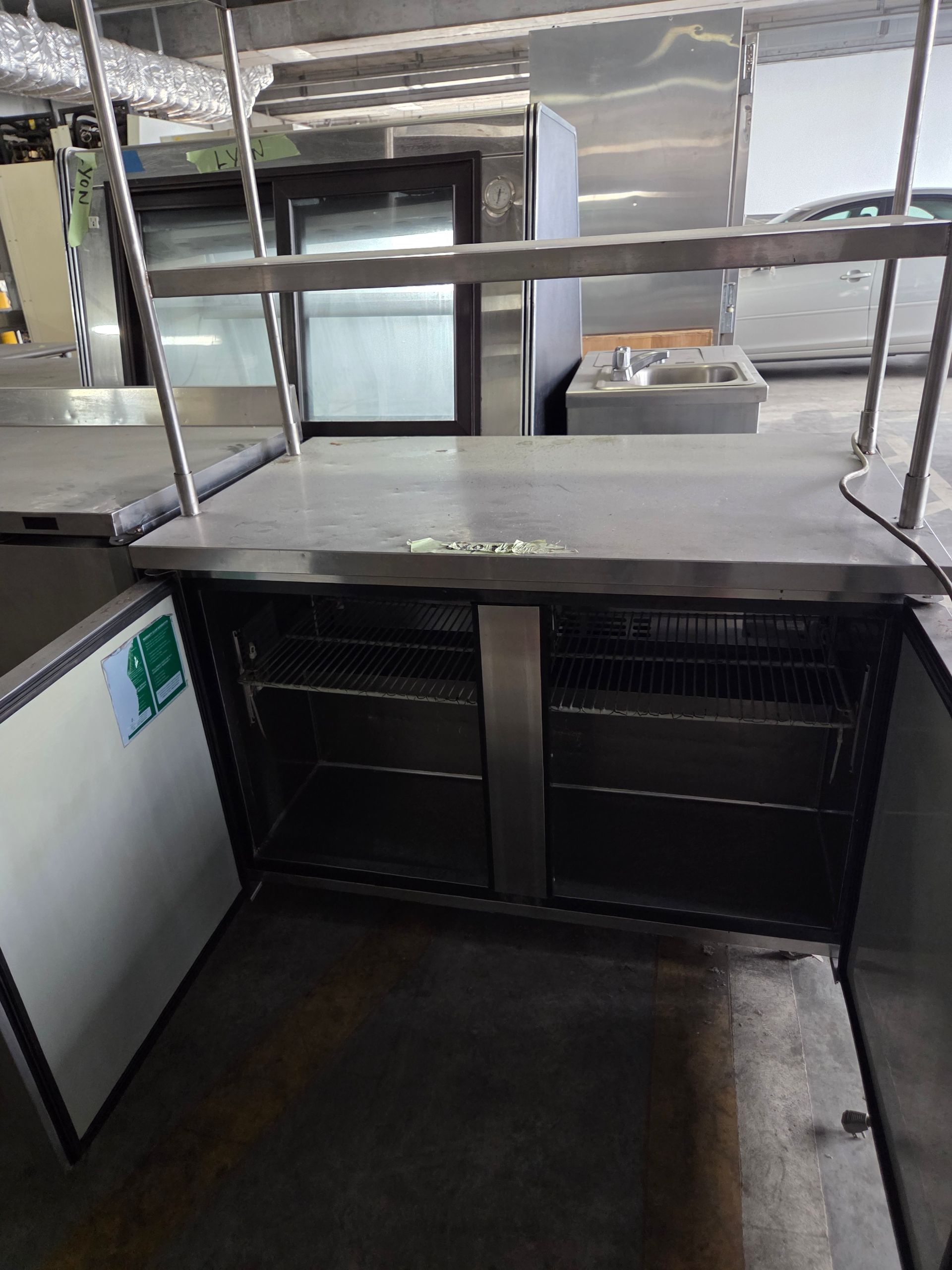 Commercial stainless steel refrigeration unit with open doors, interior shelves, and overhead shelving.