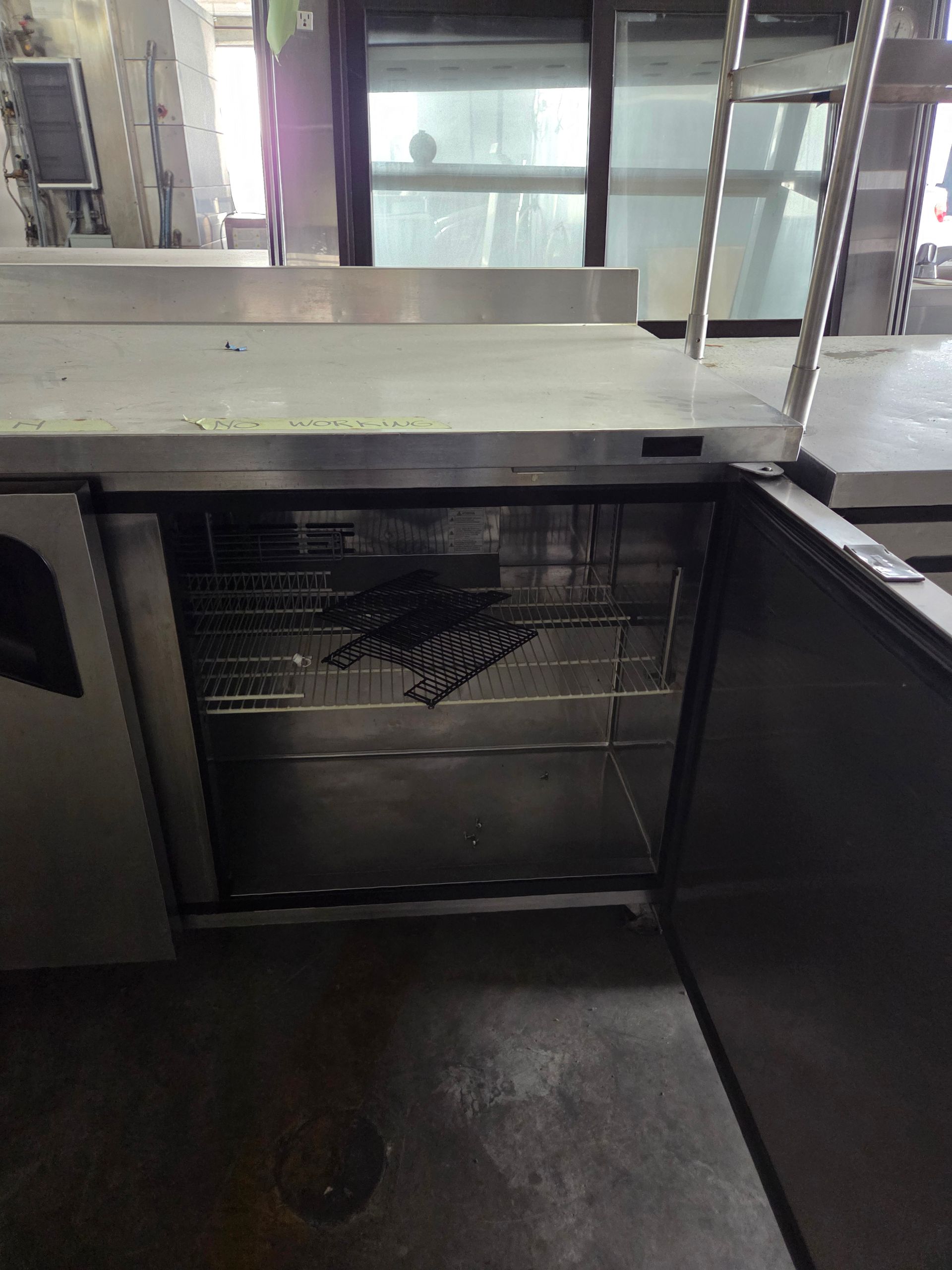 Open stainless steel commercial refrigerator under a counter, in a commercial kitchen.