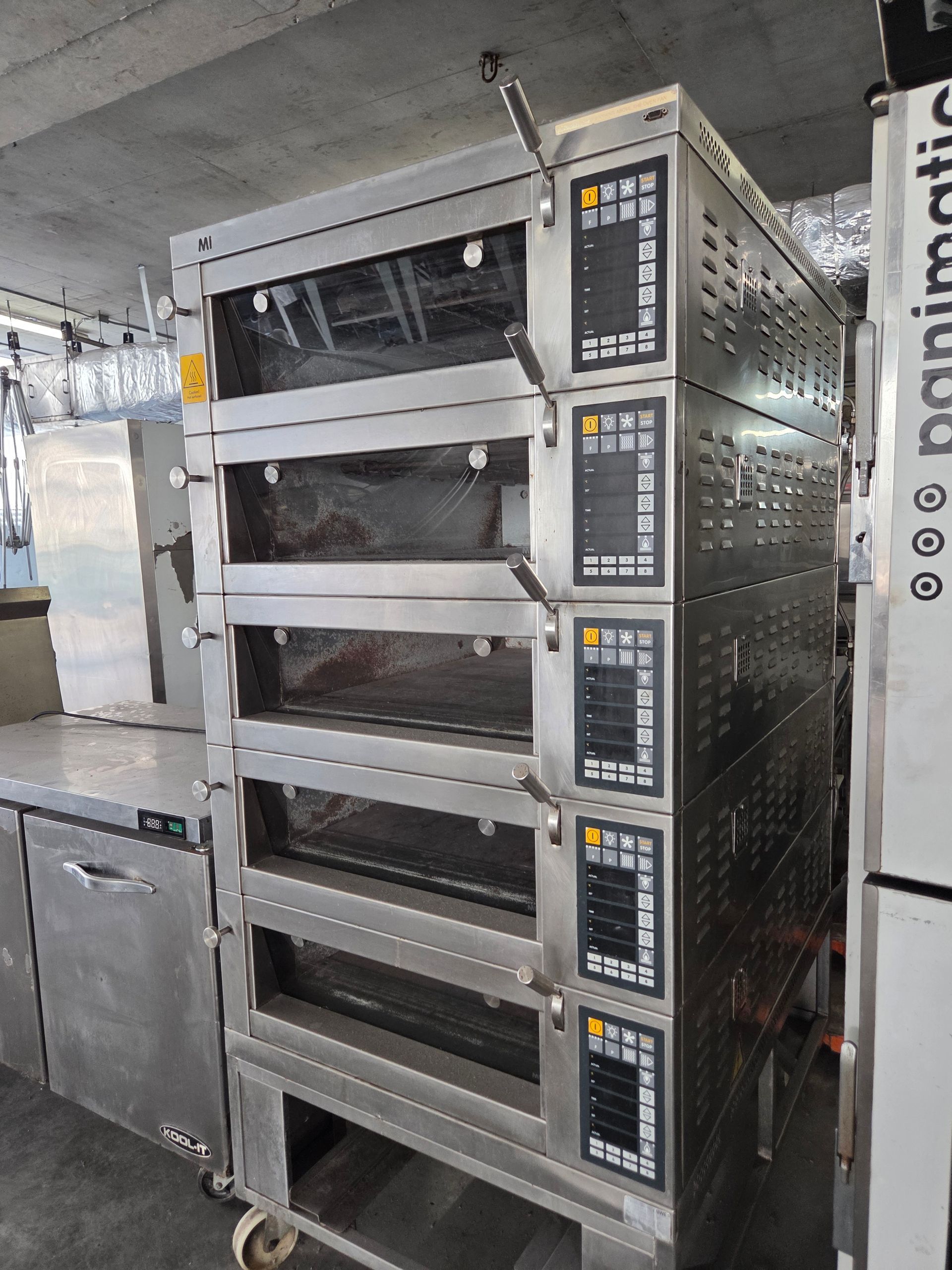 Commercial stainless steel oven with four baking chambers in a commercial kitchen.